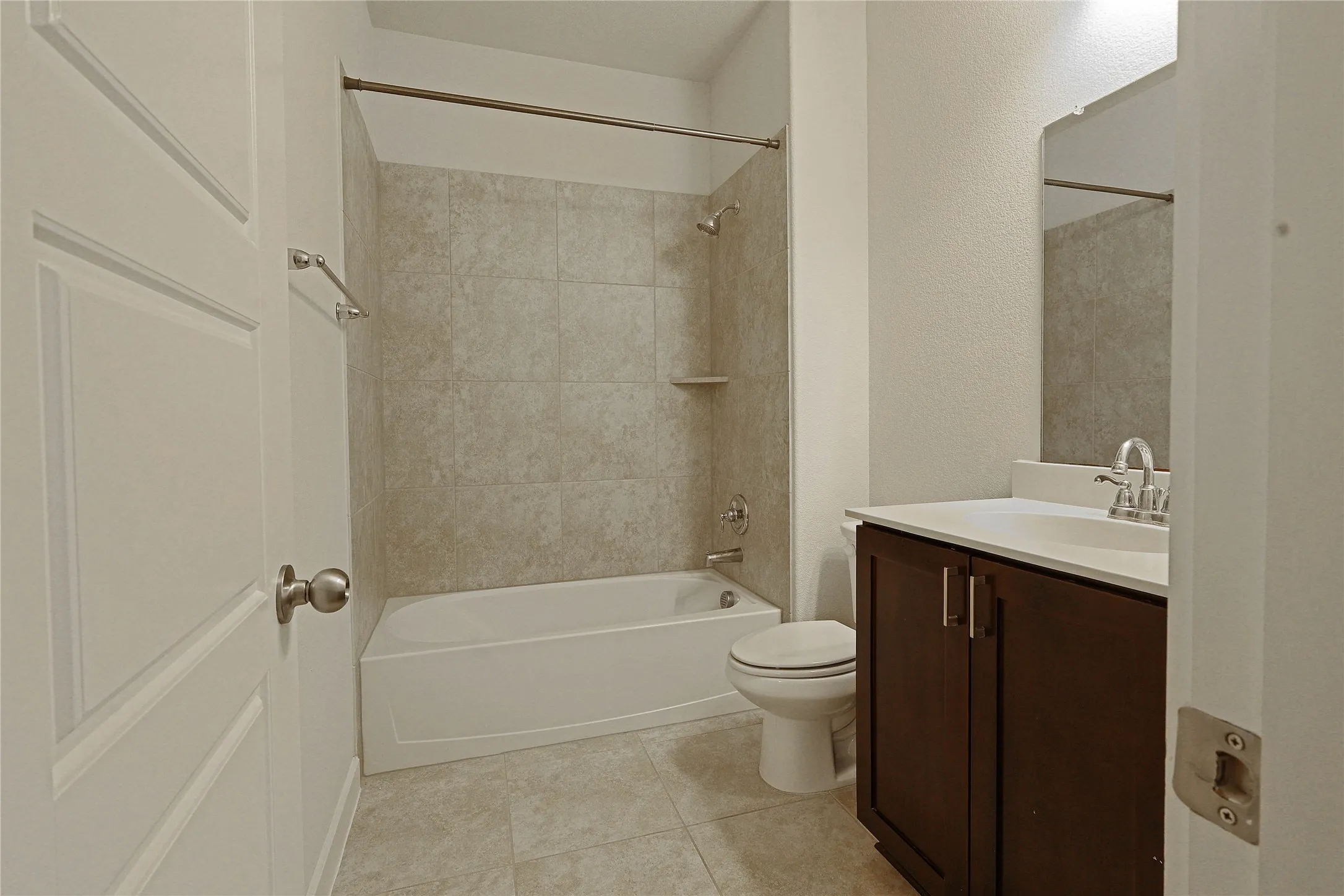 Tile flooring, vanity with dark wood-finish cabinetry, white countertop, and a shower/tub combination with tiled surround
