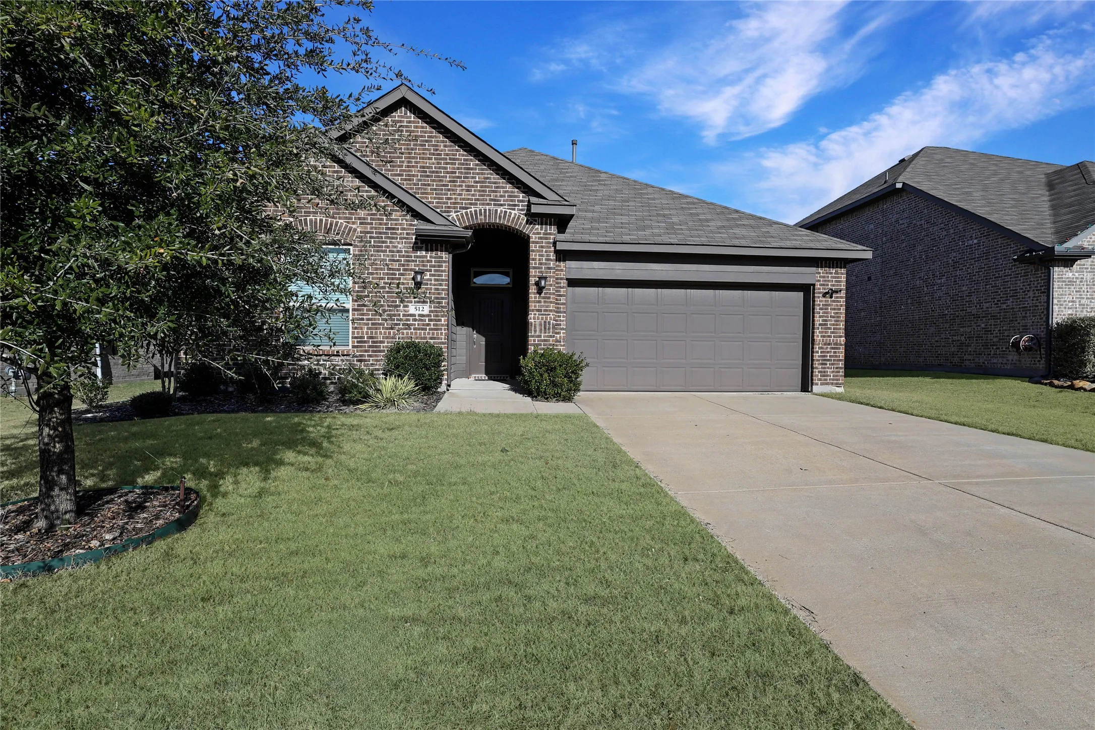 Brick exterior with a dark-toned garage door, concrete driveway, and mature landscaping