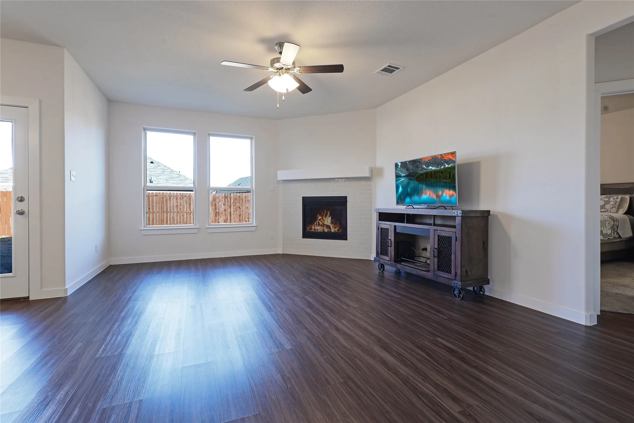 Spacious room featuring wood-finish flooring, a corner fireplace with a white mantel, and multiple windows