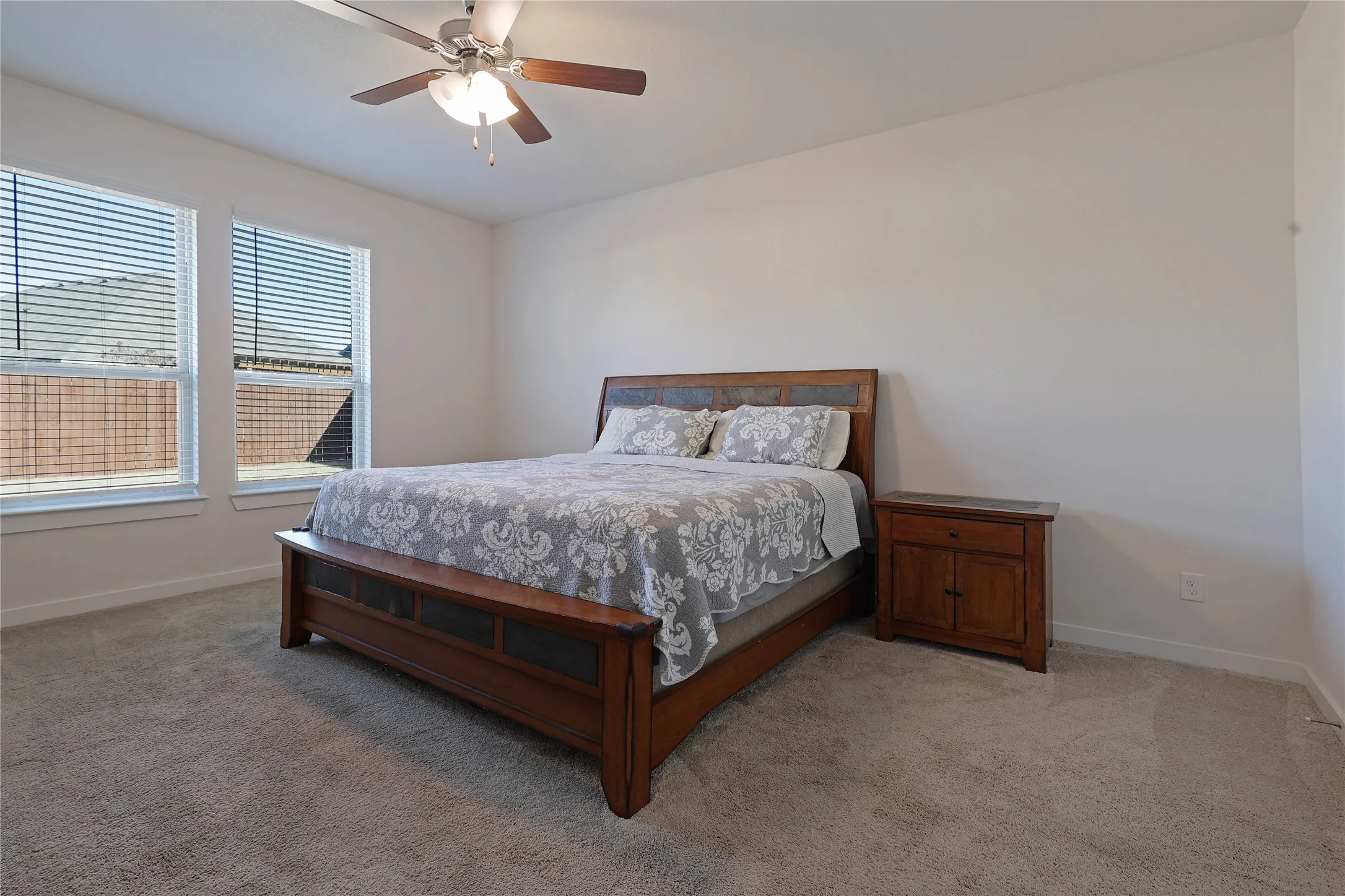 Carpeted flooring, dual windows with blinds, and a ceiling fan with integrated lighting