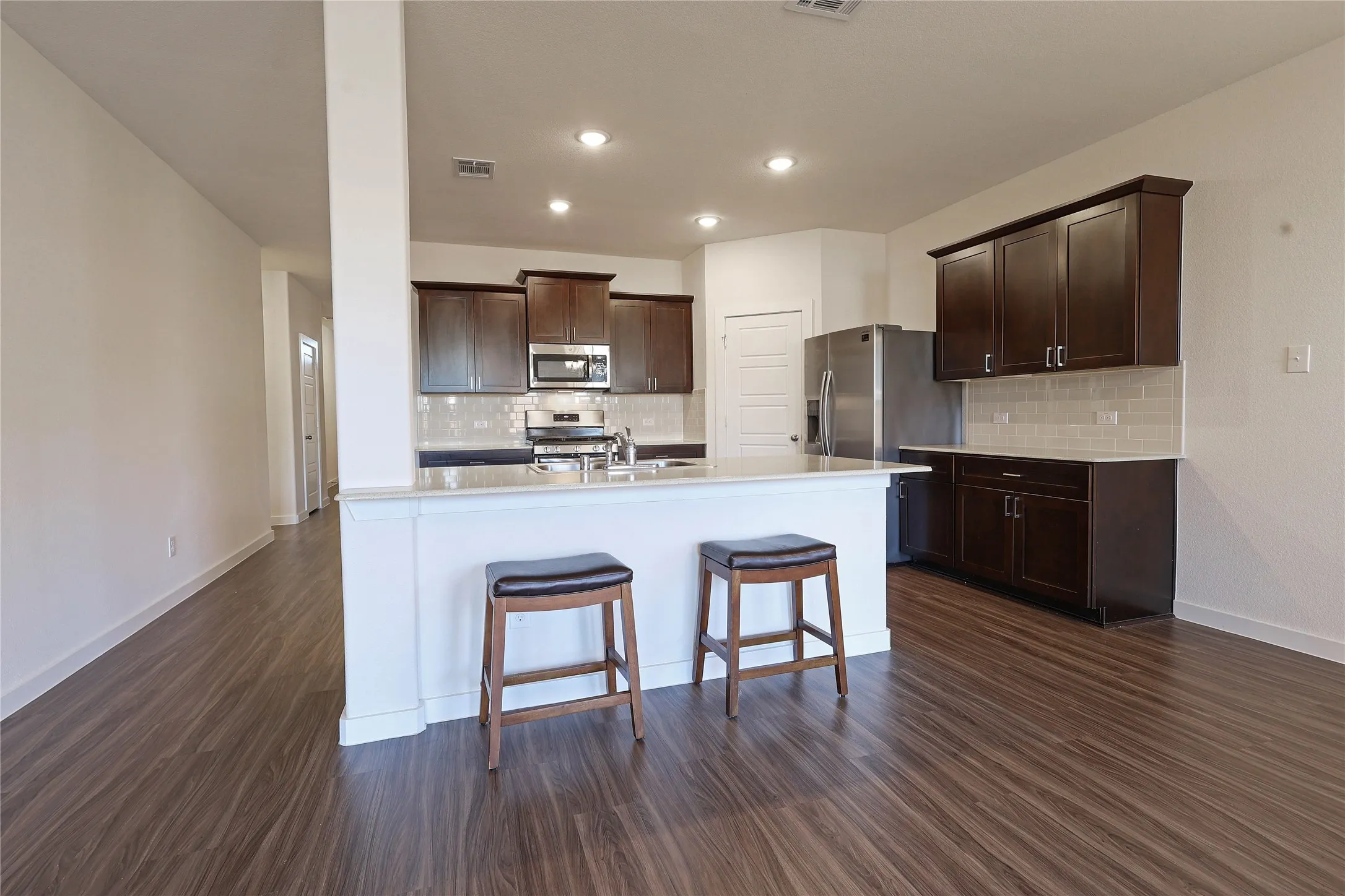Kitchen featuring wood-finish flooring, dark wood cabinetry, stainless steel appliances, a breakfast bar, and recessed lighting