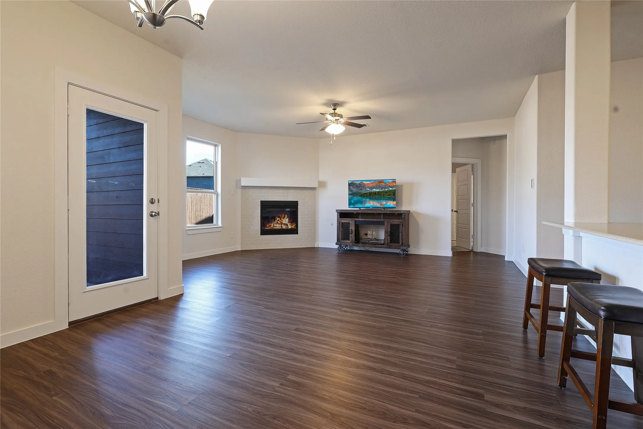 Open-concept living space featuring wood-finish flooring, a corner fireplace with a white mantel, and a ceiling fan