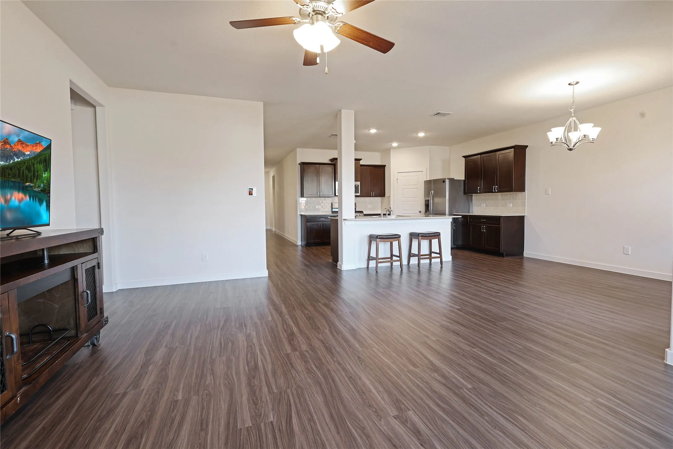 Open-concept living space with wood-finish flooring, a ceiling fan, and a chandelier