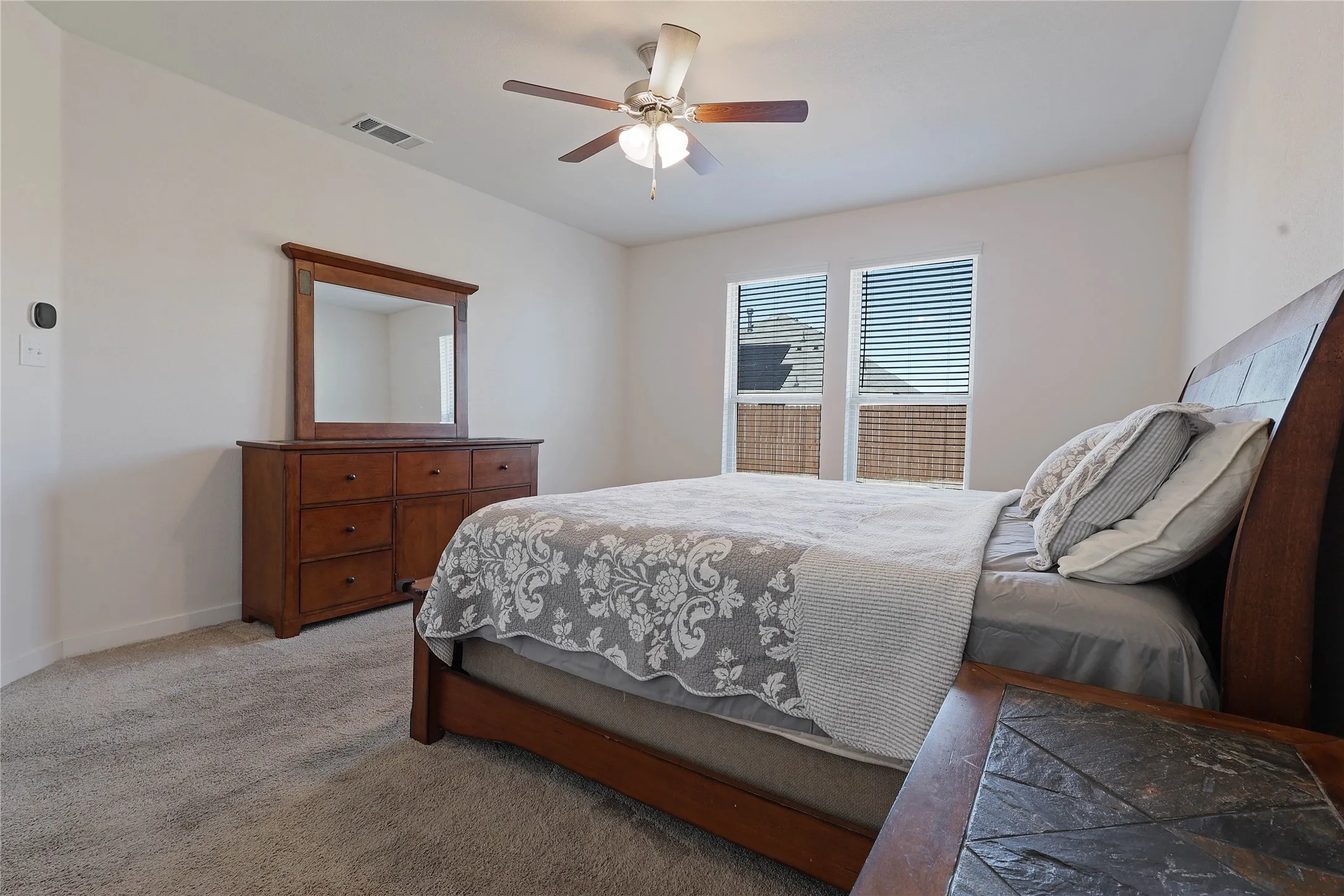 Carpeted bedroom featuring two windows with horizontal blinds, a ceiling fan with integrated lighting, and white walls