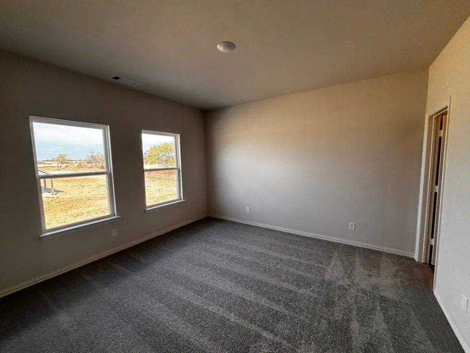 Recessed ceiling light, neutral wall paint, two windows, gray patterned carpet, and a wooden door frame