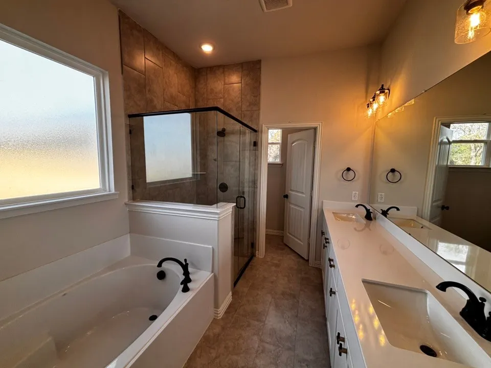 Dual vanity with integrated sinks, a built-in soaking tub, a tiled shower with glass enclosure, and modern black​​‌​​​​‌​​‌‌​‌‌​​​‌‌​‌​‌​‌​​​‌​​ fixtures