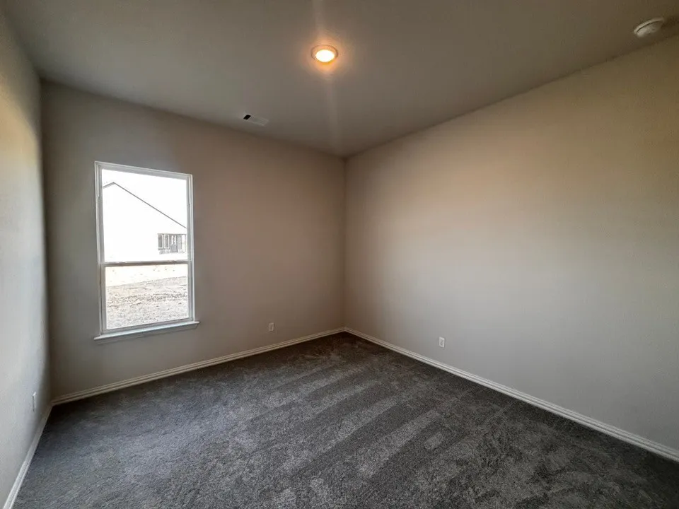 Recessed ceiling light fixture, neutral wall paint, white trim, grey patterned carpet, and a single-pane window