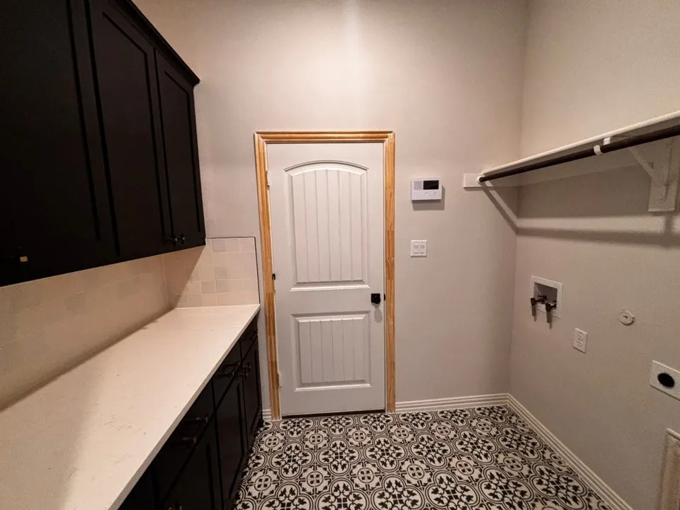 Black and white patterned tile flooring, extensive white countertop, dark cabinetry with coordinating hardware, white subway tile backsplash, and a built-in hanging rod with shelving