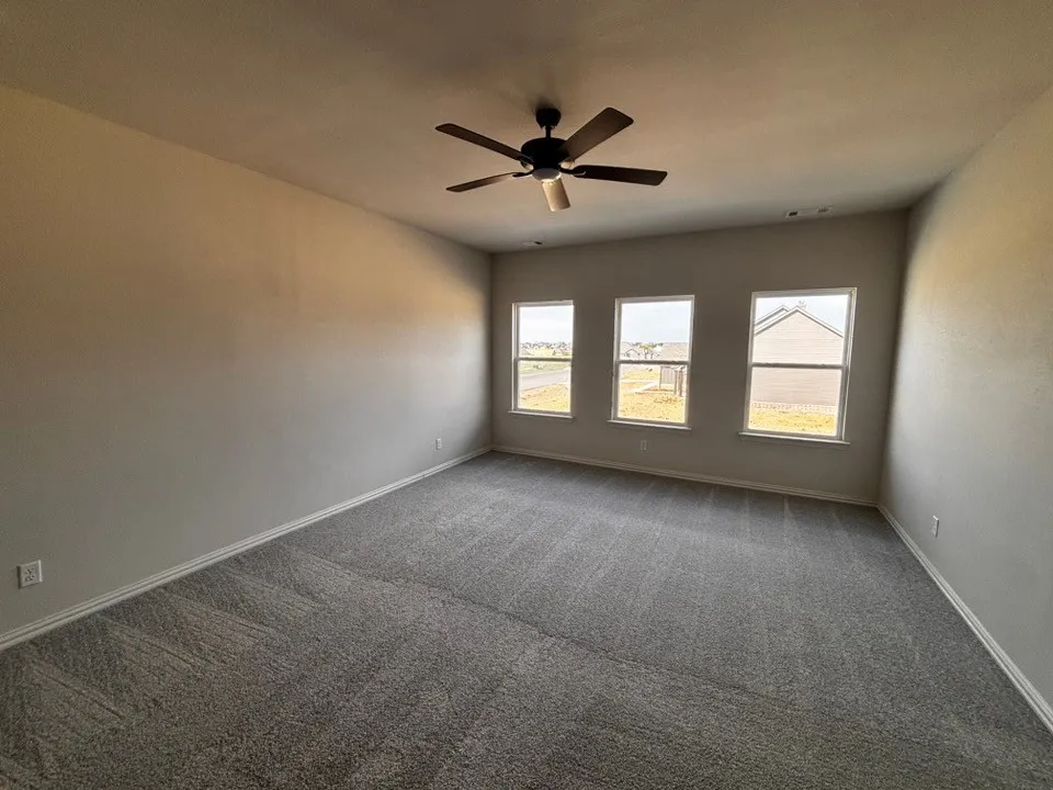 Spacious room featuring three windows, a ceiling fan, and grey carpeting