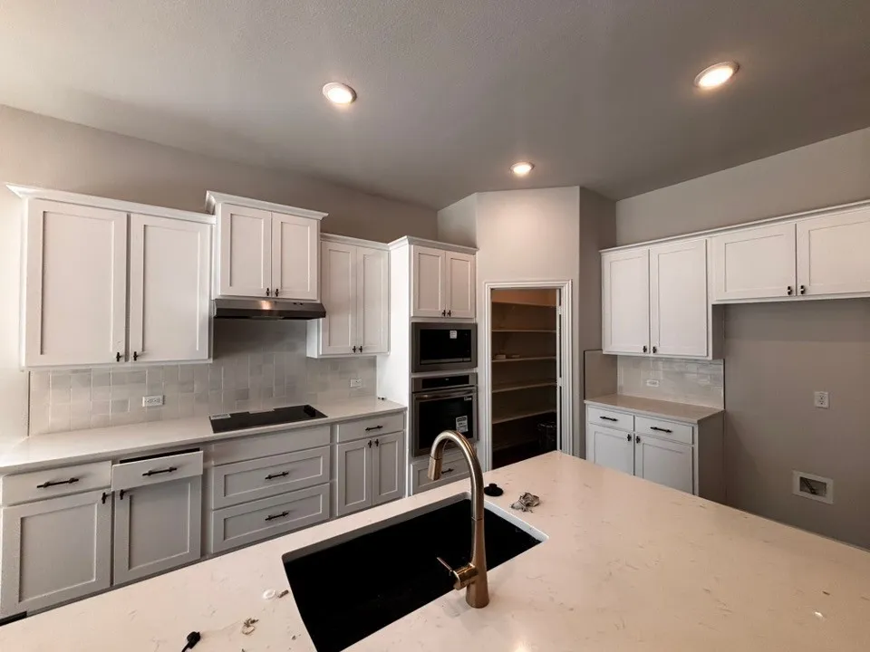 Kitchen featuring an island with an undermount sink and gold-finish faucet, white shaker-style cabinetry, stainless steel appliances, a tiled backsplash, and recessed lighting