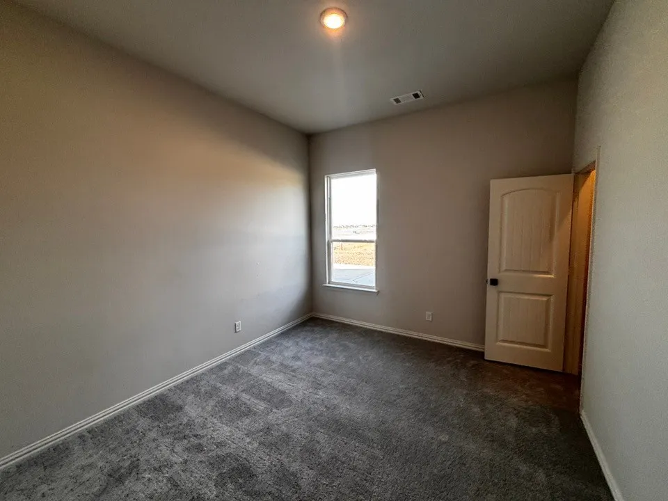 Recessed lighting, neutral wall paint, gray patterned carpeting, interior door with arch detail, and a window with a flat casing