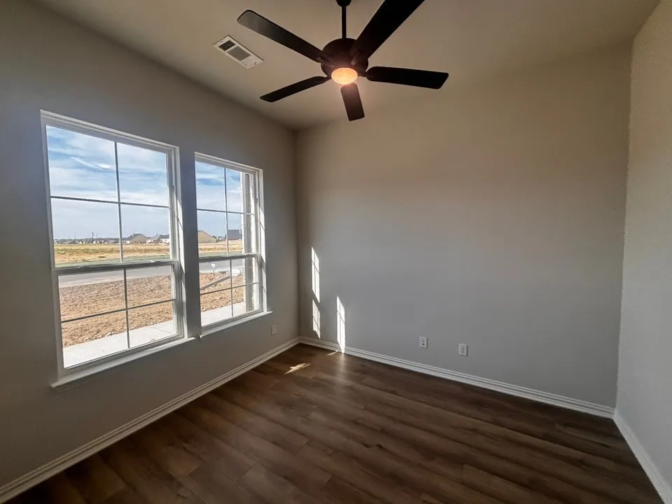Wood-finish flooring, dual windows with grid patterns, ceiling fan with integrated lighting, and neutral wall tones