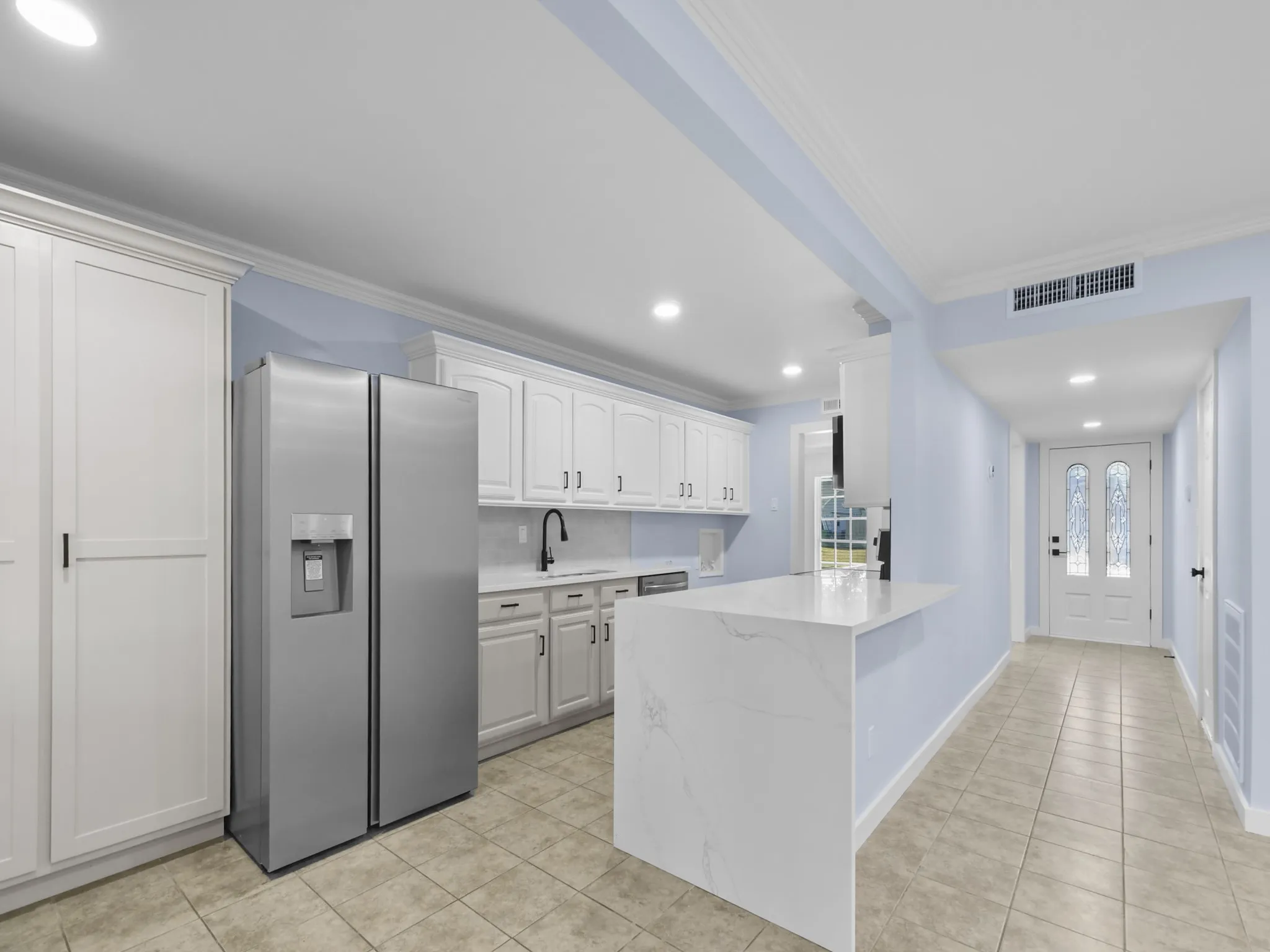 White cabinetry, light-toned tile flooring, recessed lighting, and a white entry door with decorative glass