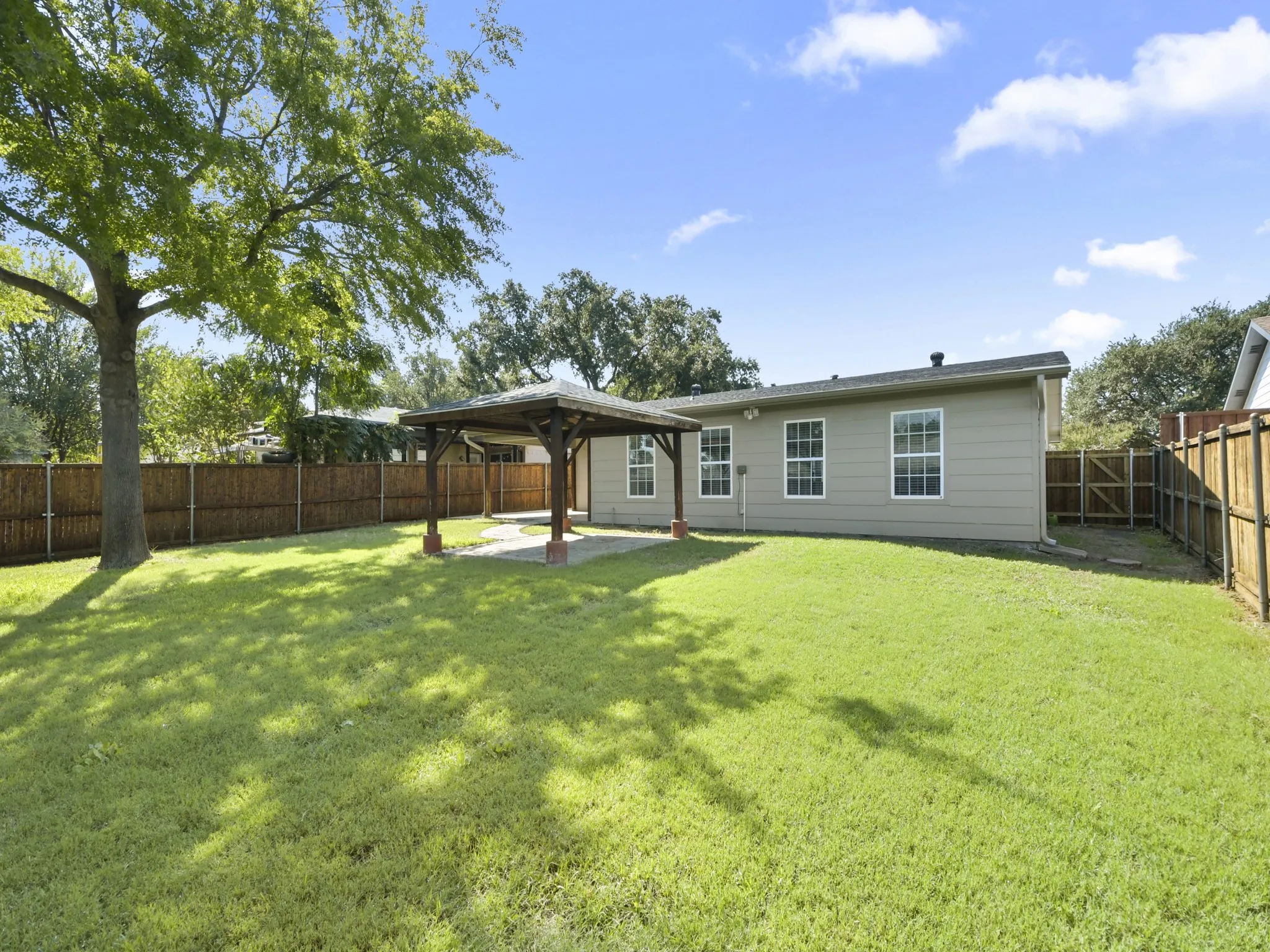 Expansive backyard featuring a lush lawn, a wood gazebo with a concrete pad, a wooden privacy fence, and a mature shade tree