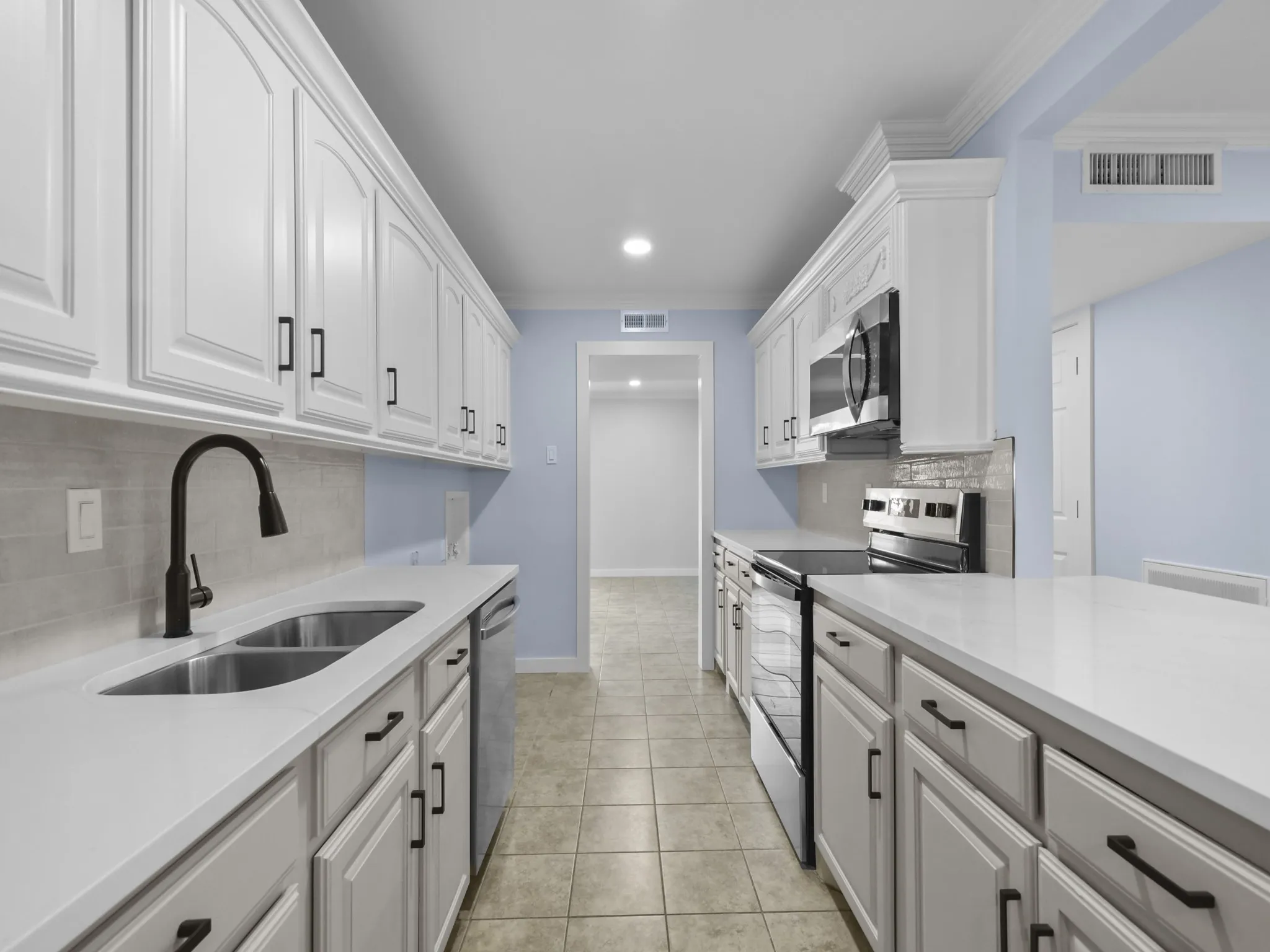 Galley kitchen featuring white cabinetry, light countertops, subway tile backsplash, and stainless steel appliances