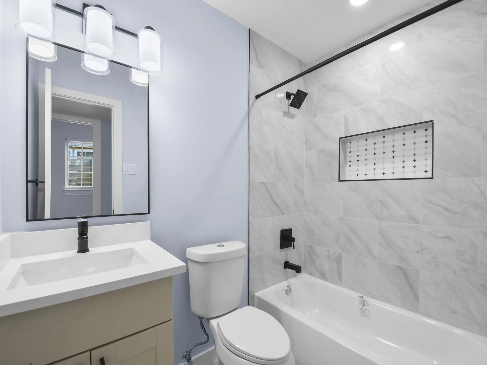 Bathroom featuring a white vanity with integrated sink, black-framed mirror, and a light fixture with opaque cylindrical shades