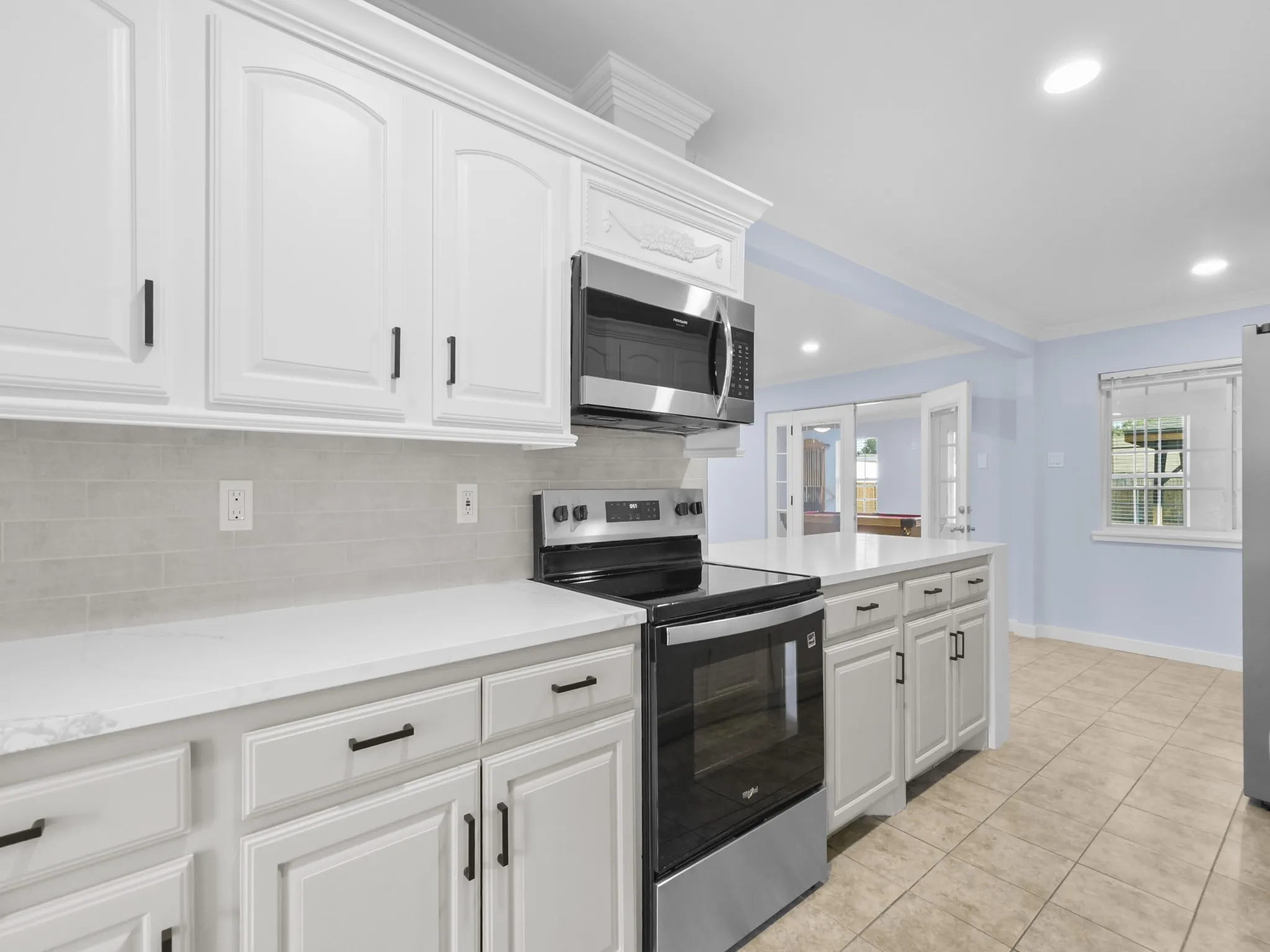 White cabinetry with matte black hardware, stainless steel appliances, light gray subway tile backsplash, white countertops, and neutral tile flooring
