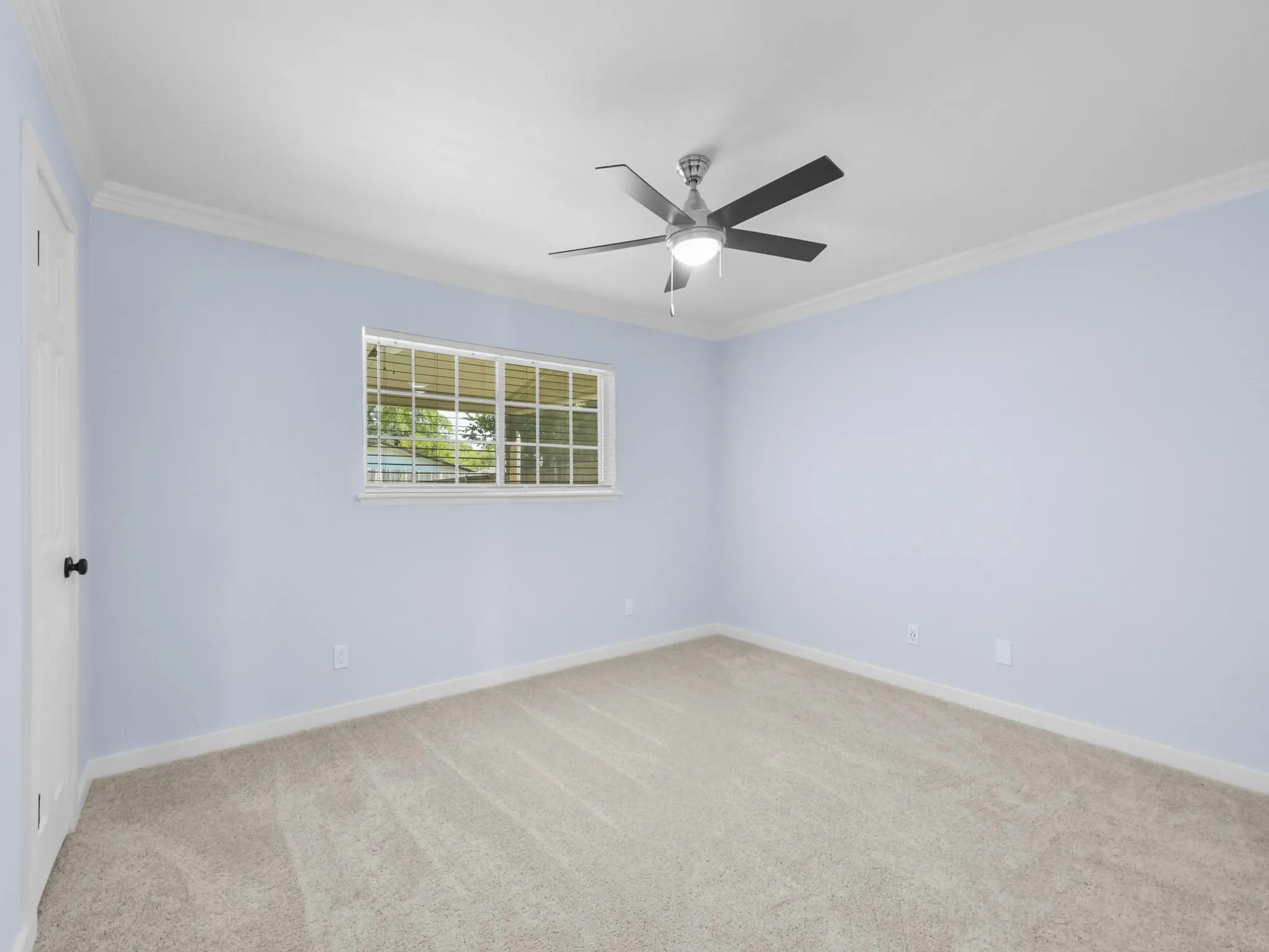 Recessed window with blinds, ceiling fan with integrated lighting, door with black hardware, crown molding, and neutral carpet flooring