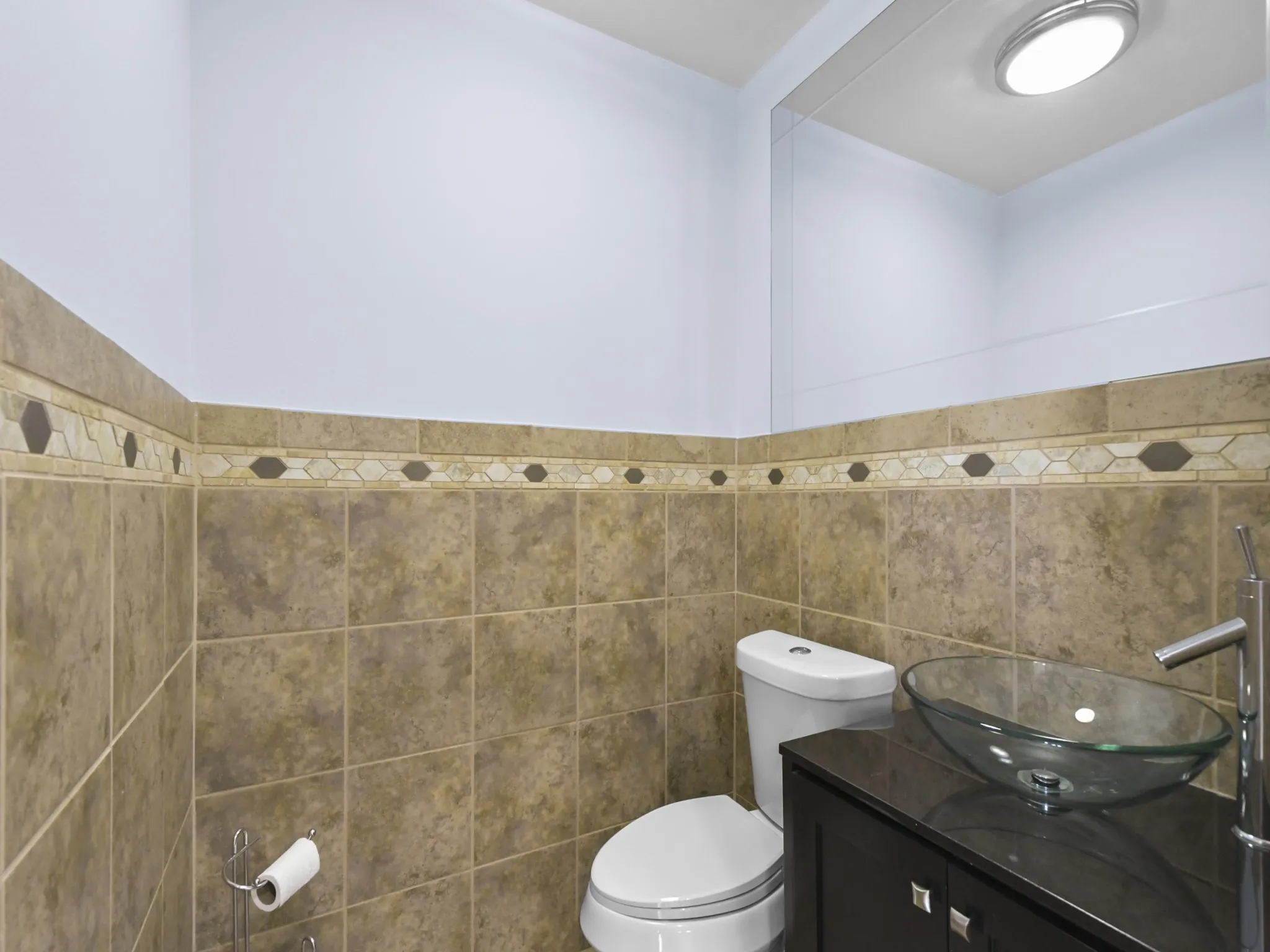 Half Bath - Tiled walls with decorative band, modern vessel sink, dark wood-finish vanity, and integrated mirror