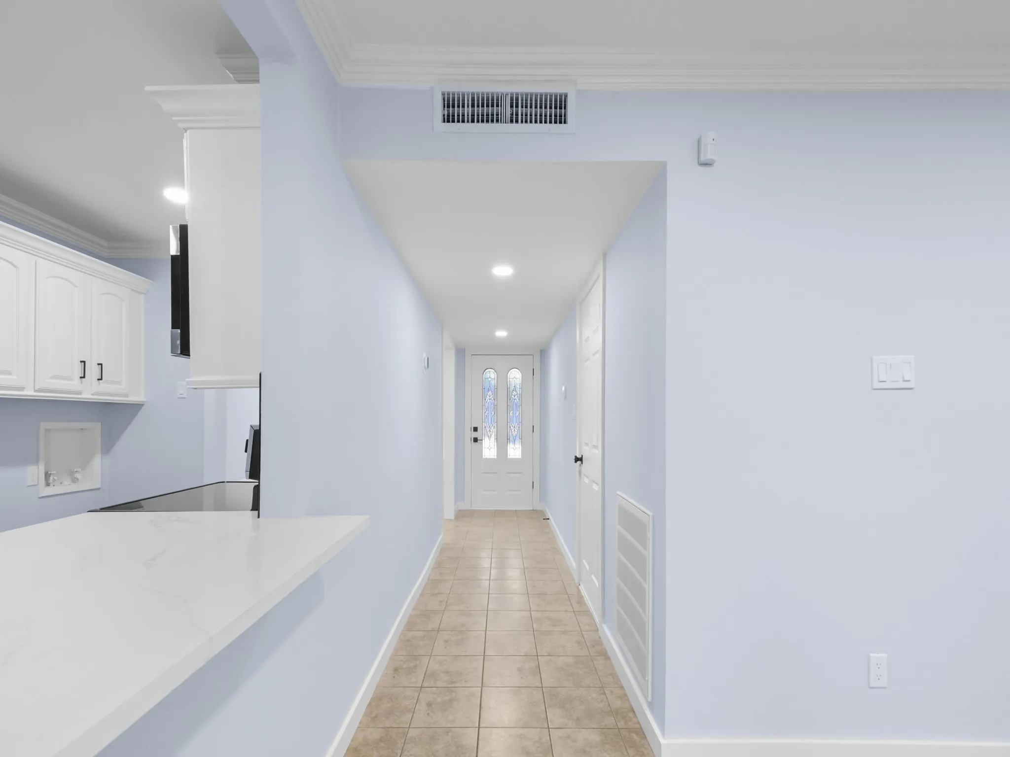 Light-toned ceramic tile flooring, recessed lighting, crown molding, white shaker cabinetry, and a white countertop