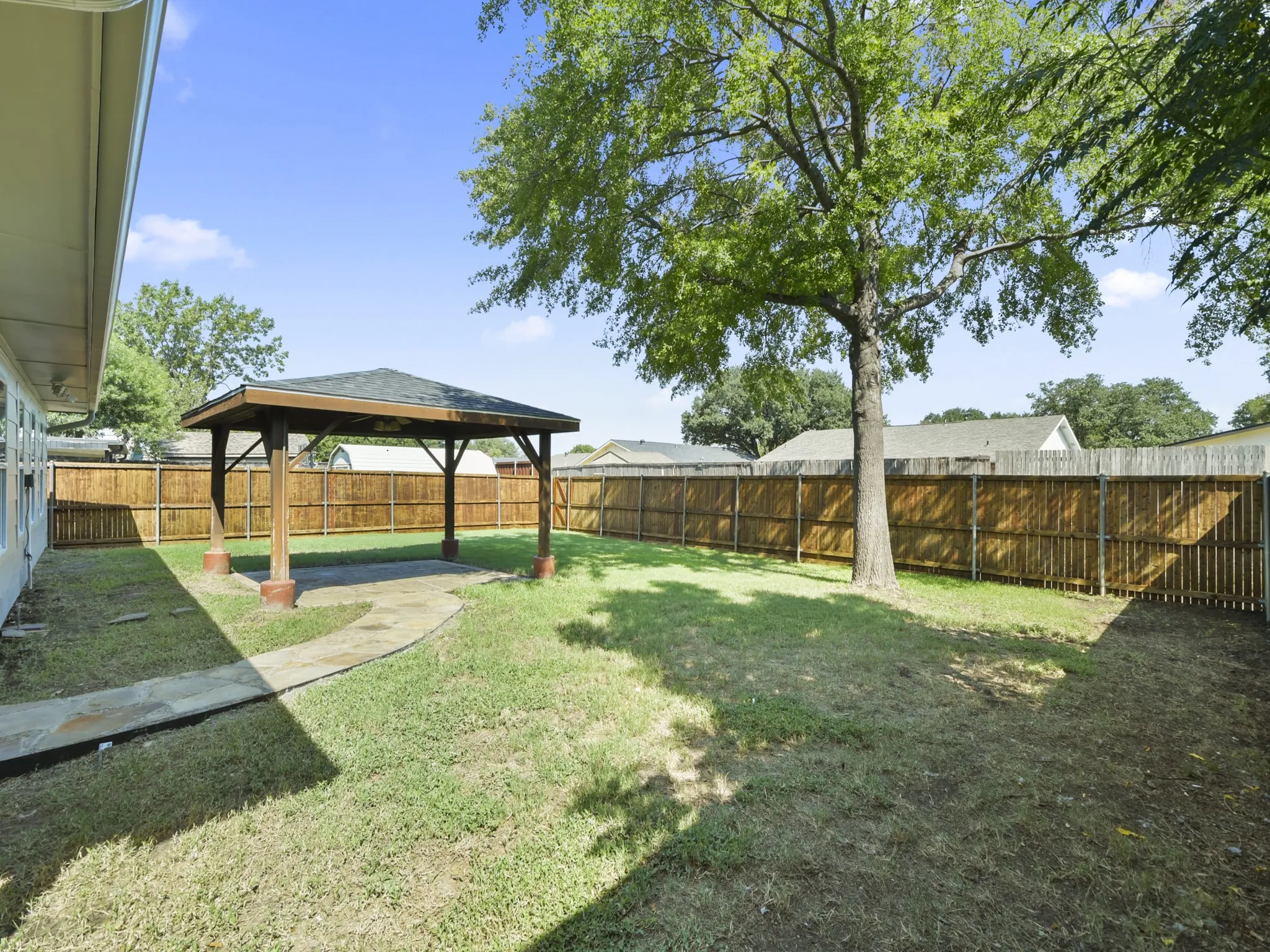 Expansive backyard featuring a wood gazebo with a shingle roof, a stone pathway, mature trees, and a full privacy fence