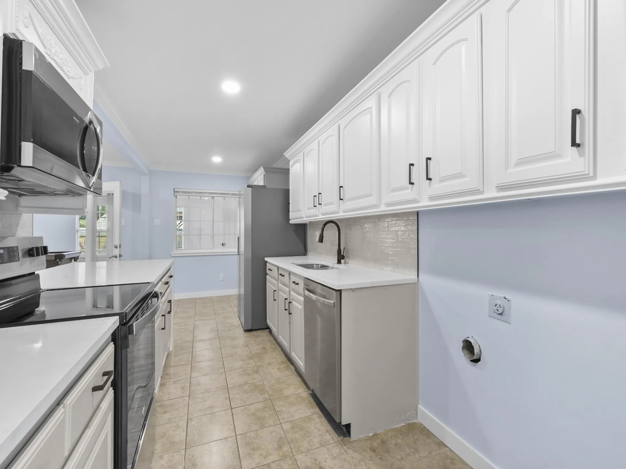 White cabinetry with dark hardware, stainless steel appliances, light-colored countertops, and tile flooring