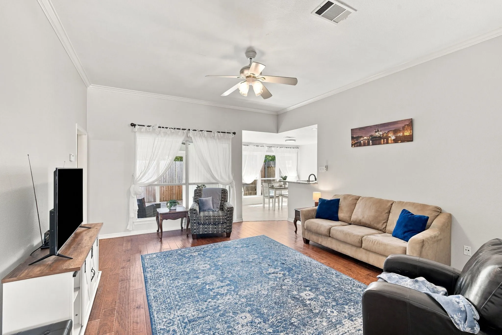 A cozy living area featuring engineered wood flooring, vaulted ceilings, crown molding and plentiful natural lighting