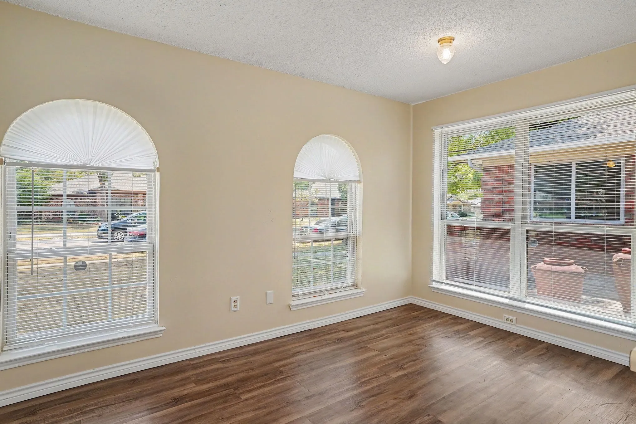 Wood-finish flooring, two arched windows, a large rectangular window, and a flush mount ceiling light fixture