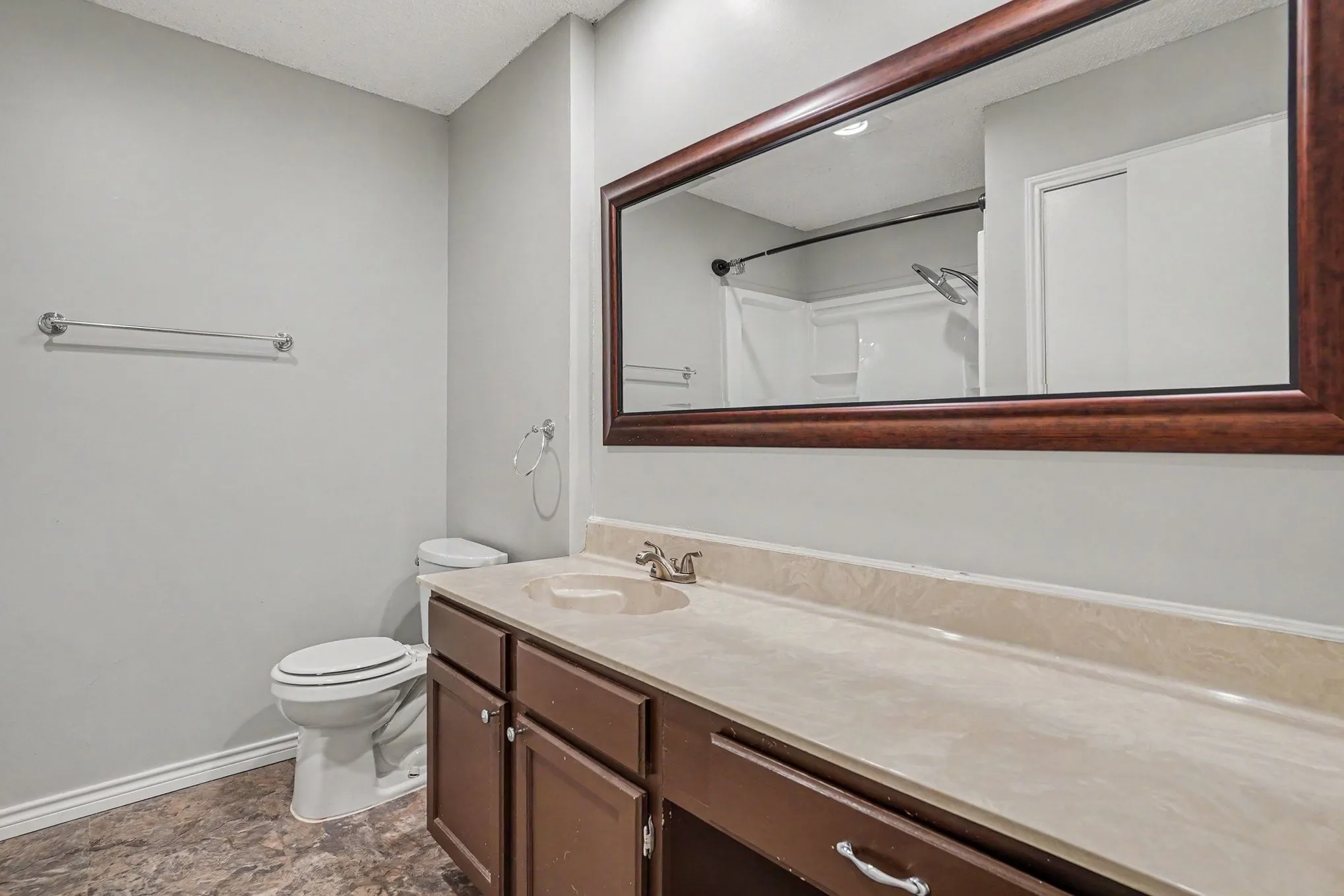 Bathroom vanity with an integrated sink, a wood-framed mirror, and a shower with a curtain rod