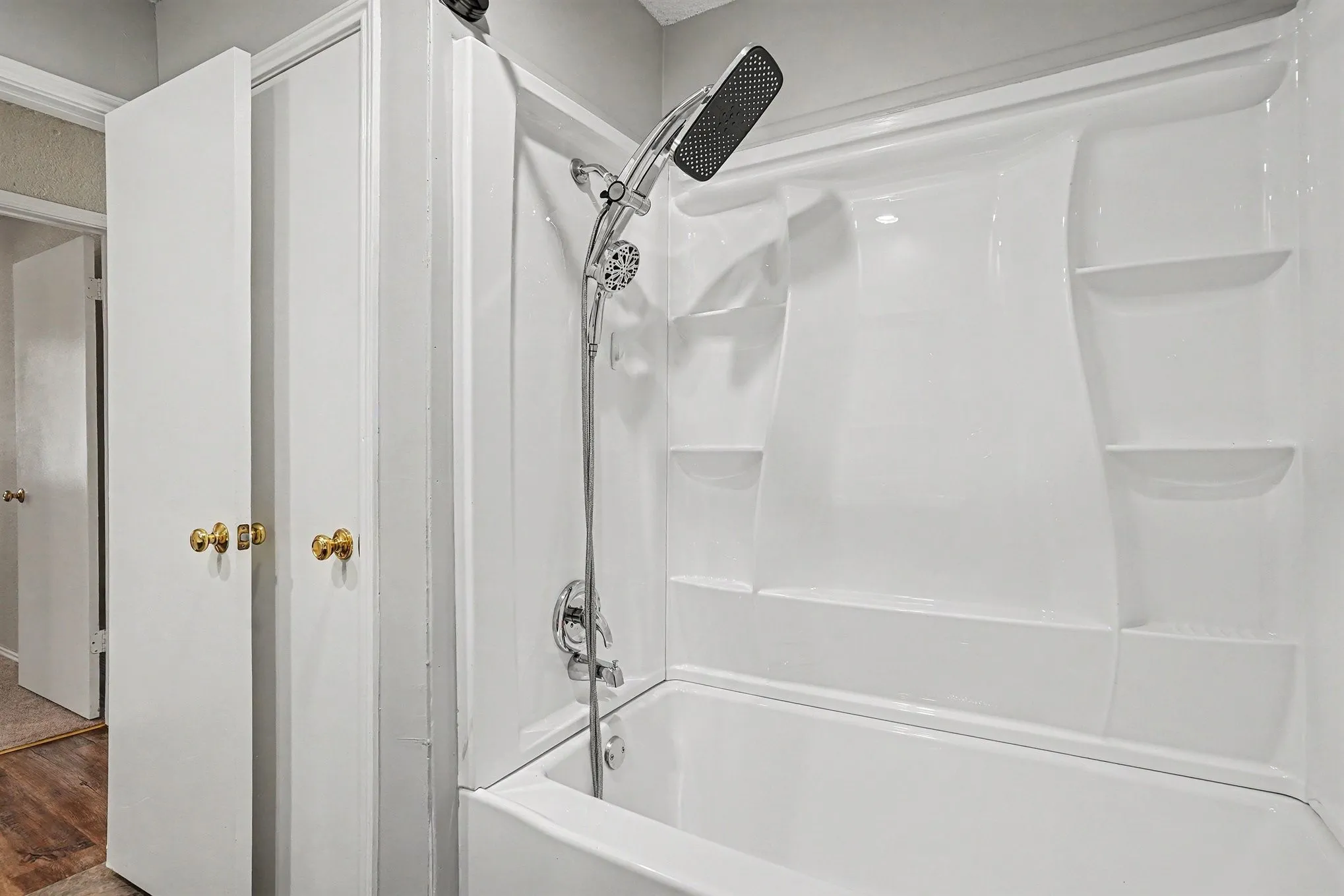 White fiberglass tub and shower combination with integrated shelving