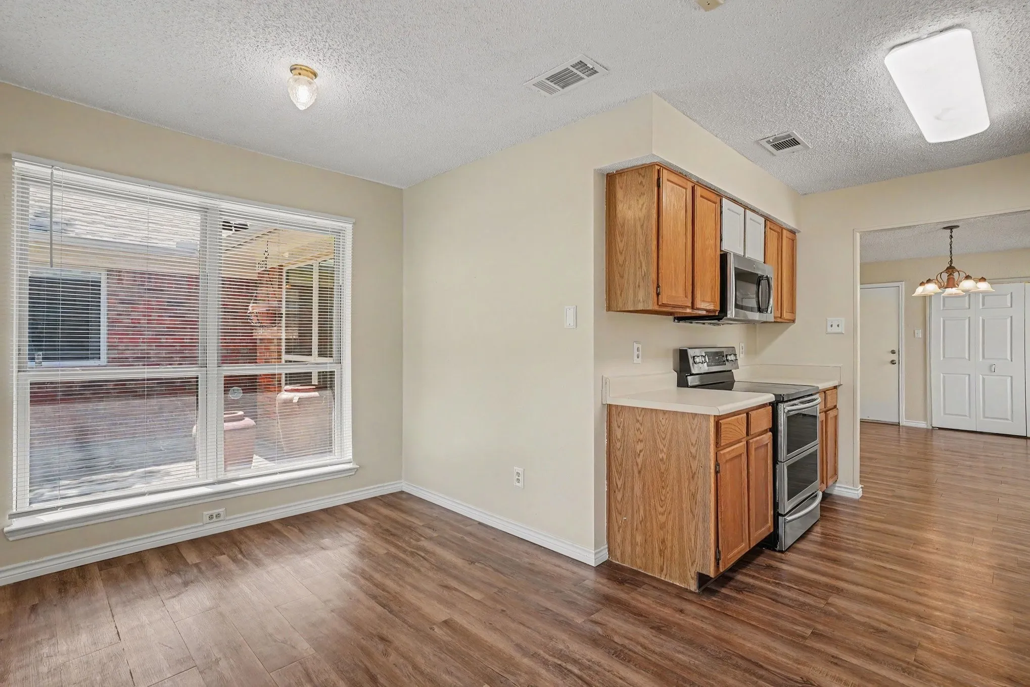 Wood-finish flooring, full-lite window, wood cabinetry, stainless steel microwave, and stainless steel oven