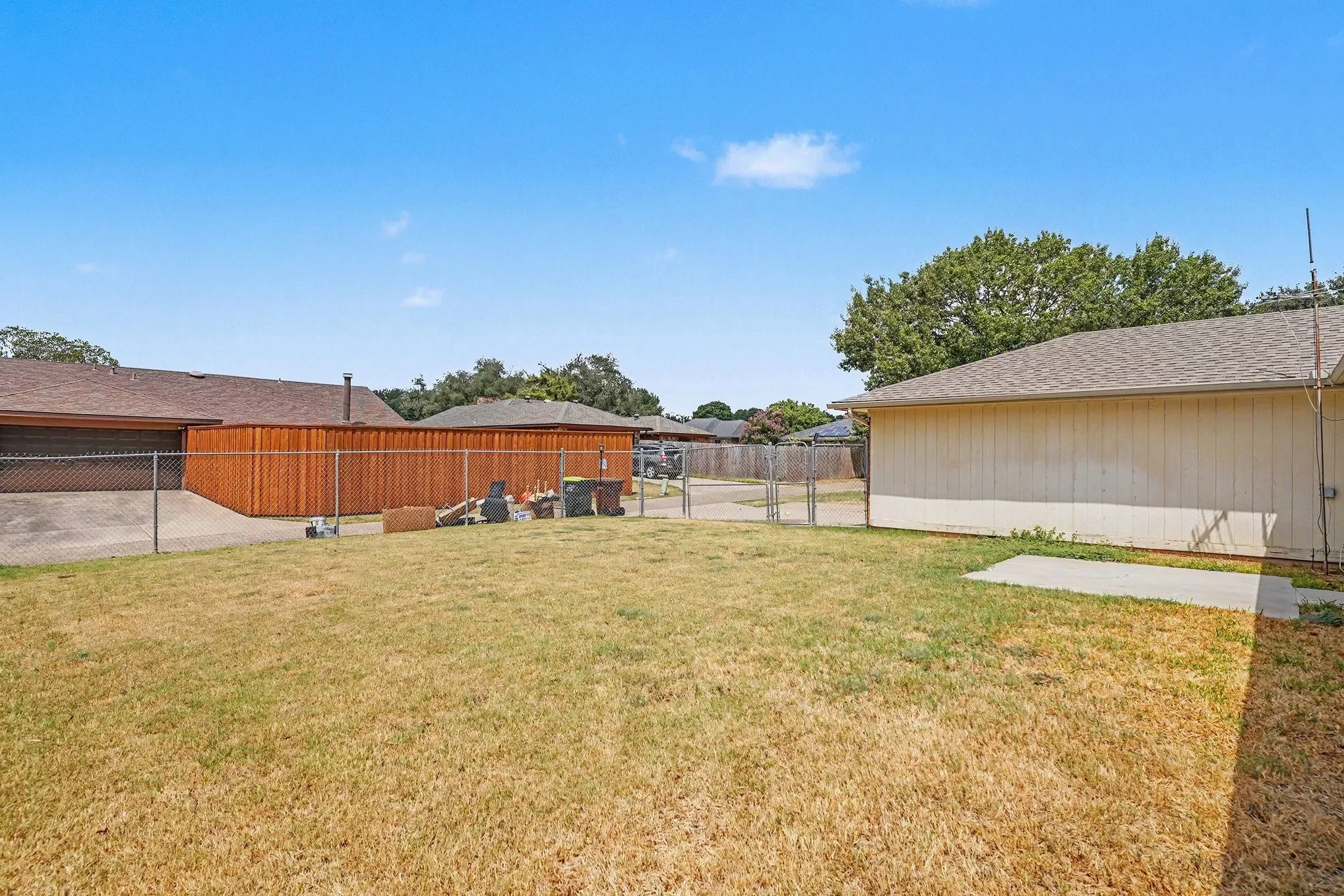 Expansive backyard with a chain-link fence, concrete patio, and mature trees