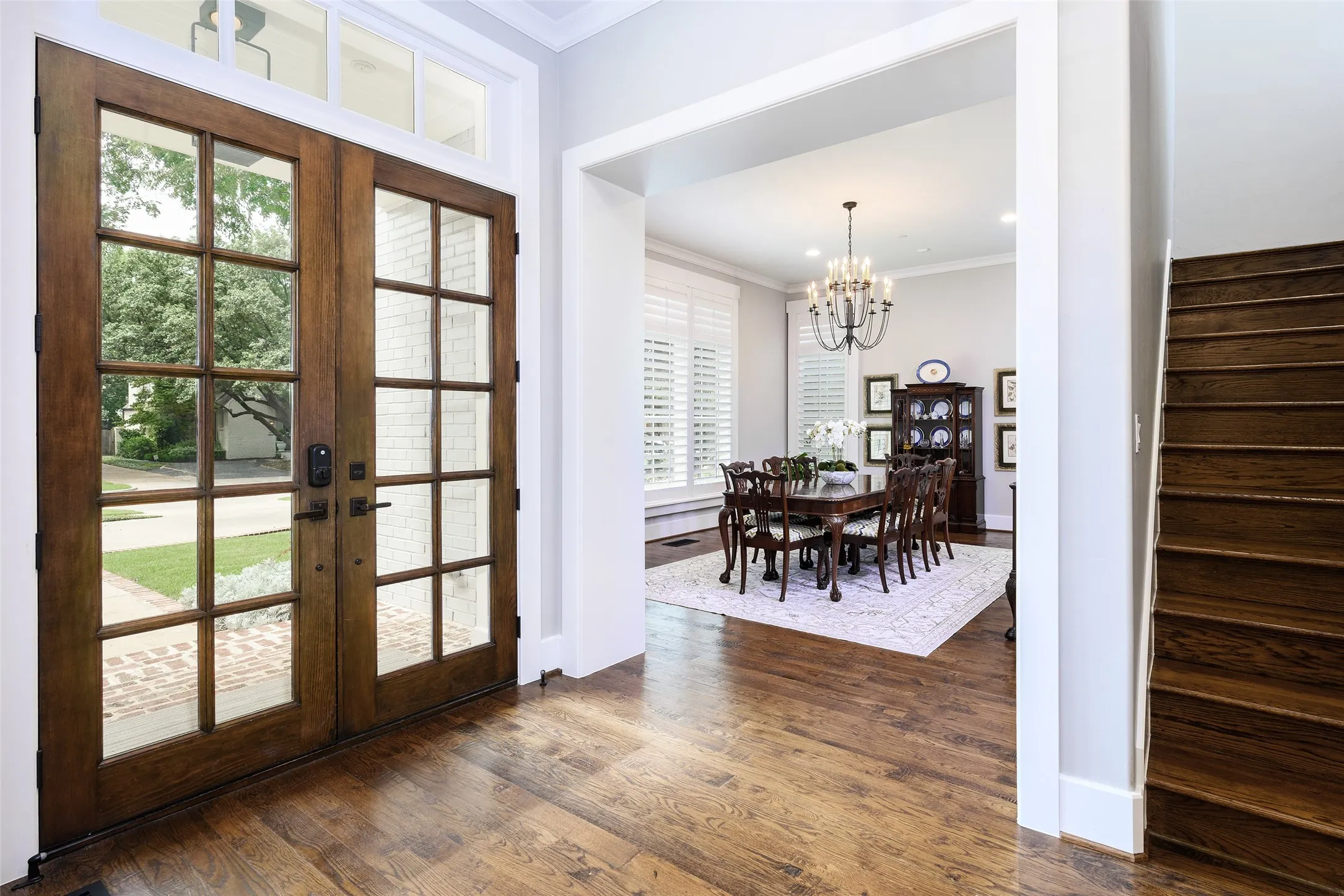 Wood-finish flooring throughout the entry, double front doors with transom, and a dedicated dining space featuring a chandelier and window shutters