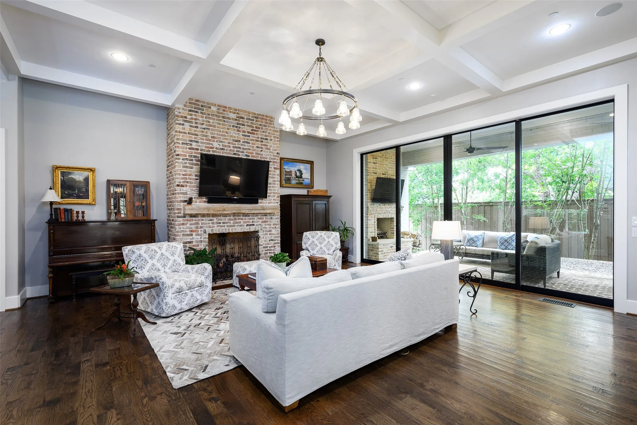 Exposed brick fireplace with a wood mantel, coffered ceiling, wood-finish flooring, recessed lighting, and expansive sliding glass doors