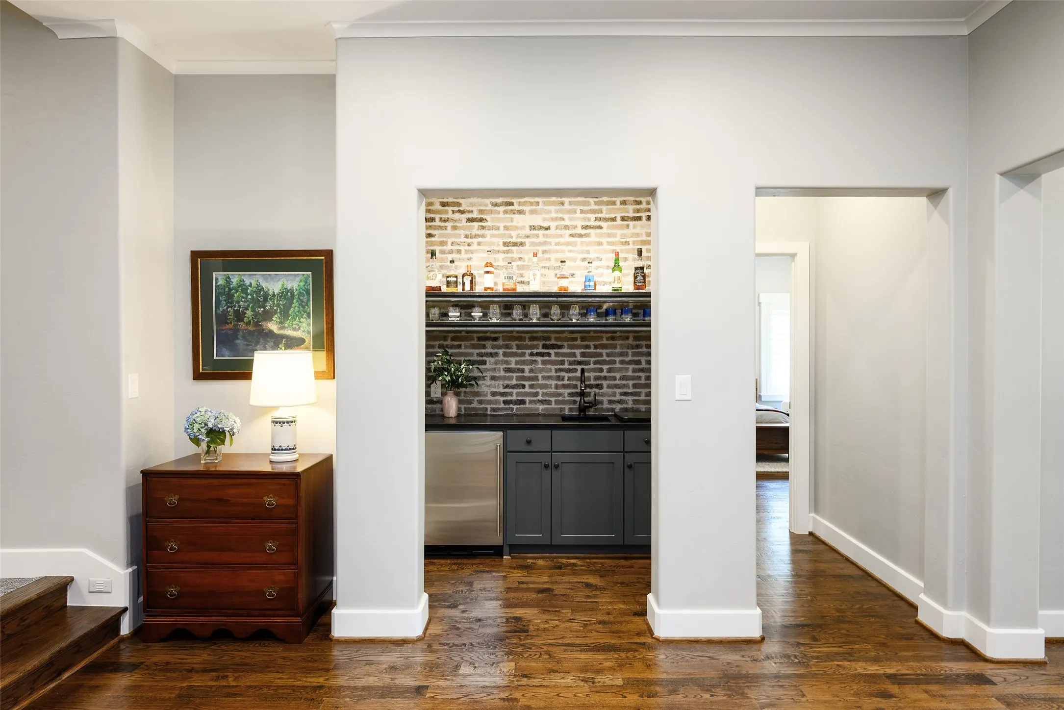 Built-in wet bar featuring a brick accent wall, stainless steel beverage refrigerator, dark cabinetry, and a dark countertop