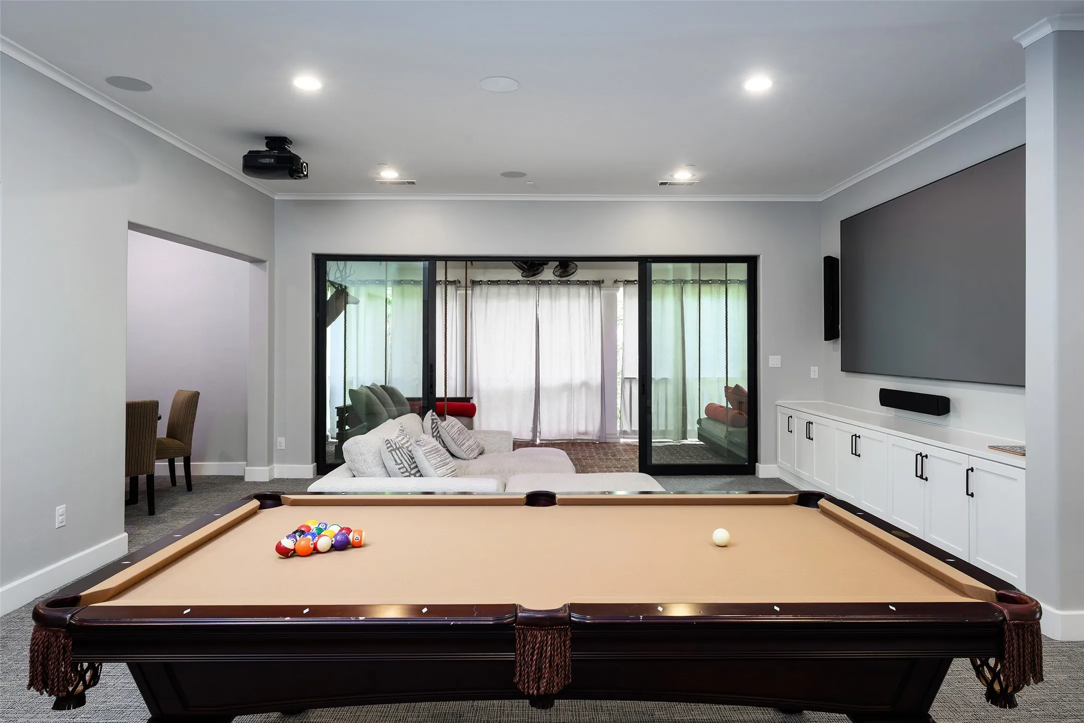 Recessed lighting, built-in cabinetry with dark hardware, large wall-mounted screen, and sliding glass doors