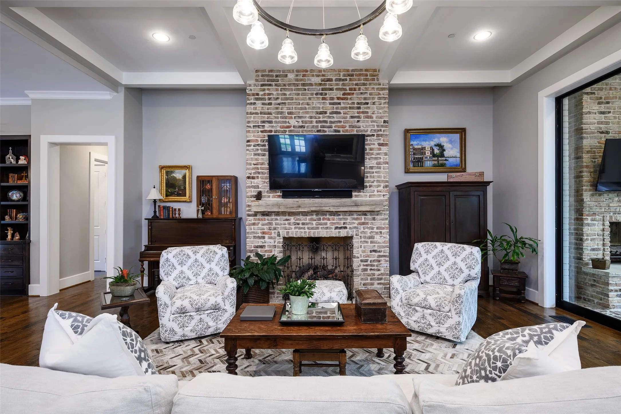 Exposed brick fireplace with a wood-mantel, tray ceiling, recessed lighting, and wood-finish flooring