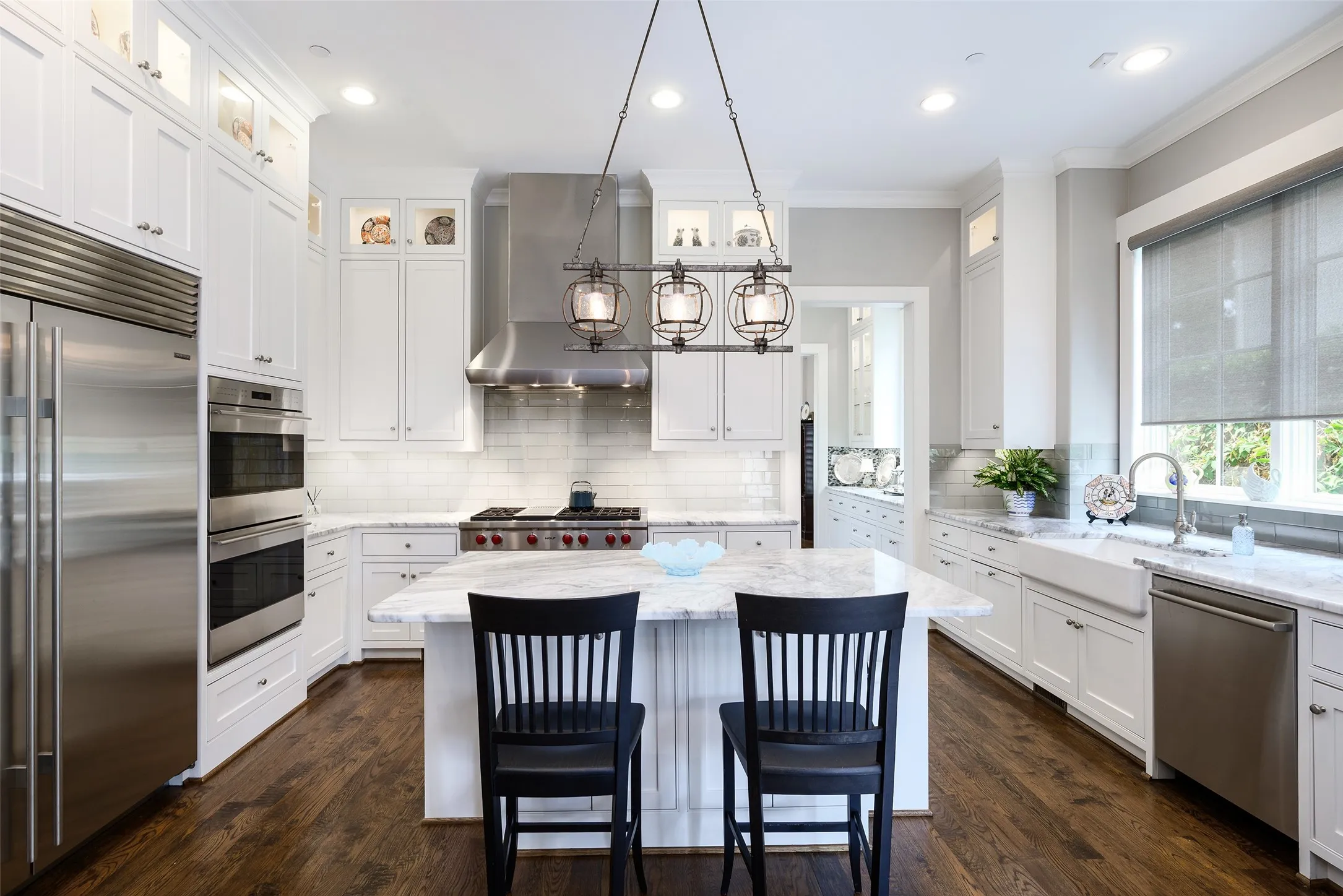 Gourmet kitchen featuring white cabinetry, stainless steel appliances, a center island with countertop seating, a farmhouse sink, and wood-finish flooring