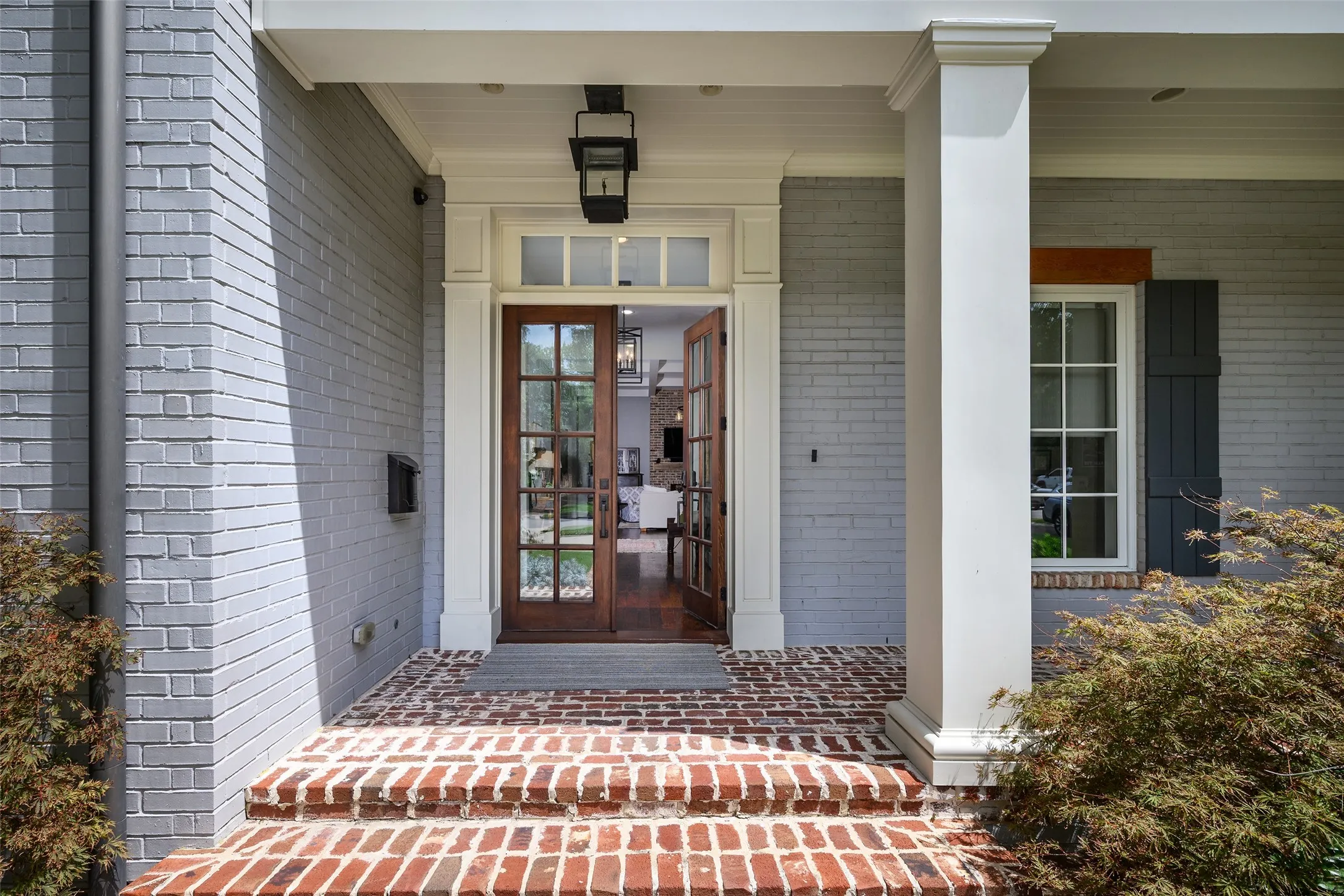 Painted brick exterior with a columned front porch, brick steps, and wood-finish French doors
