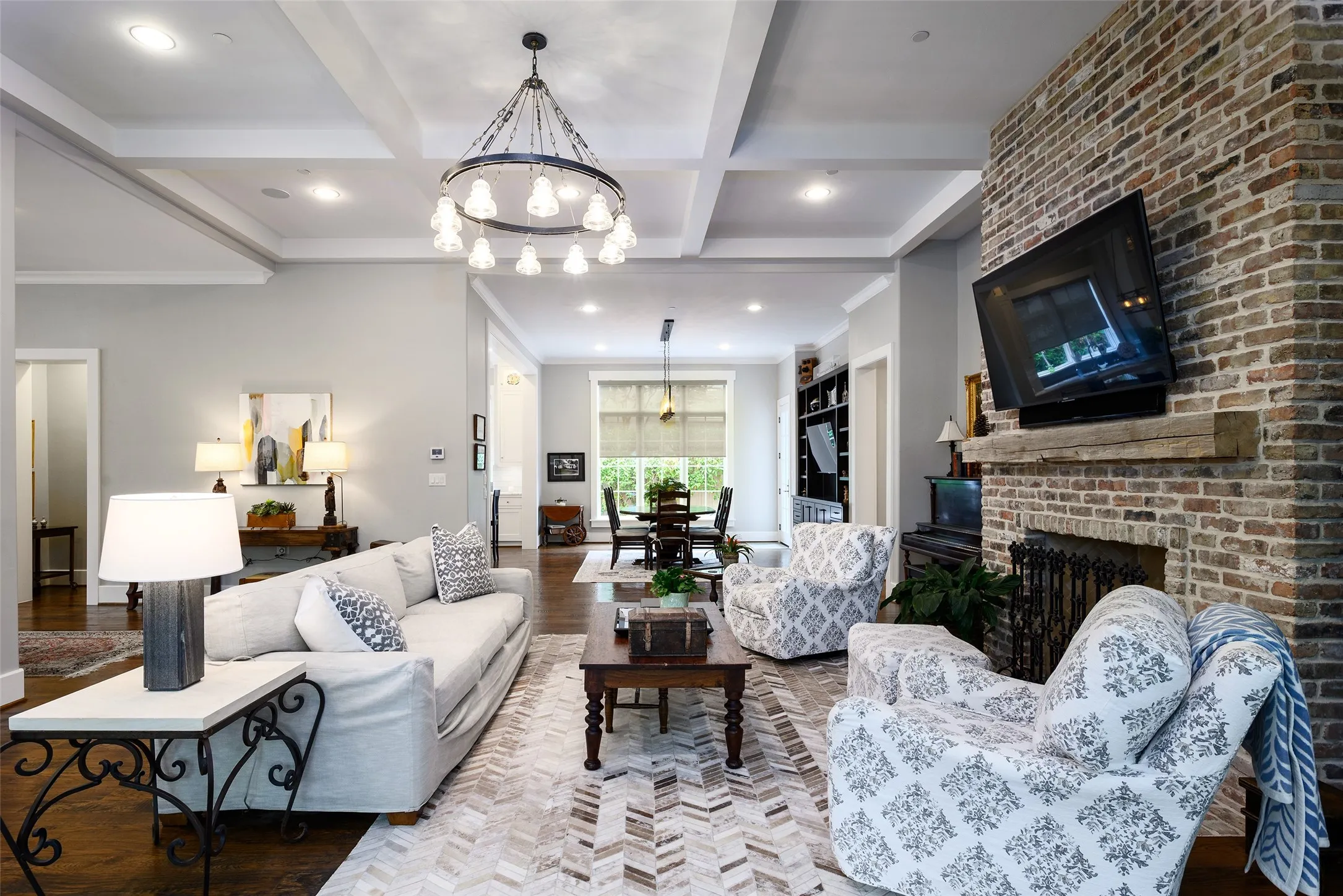 Coffered ceiling, overhead chandelier, brick fireplace with stone mantel, recessed lighting, and dark wood flooring