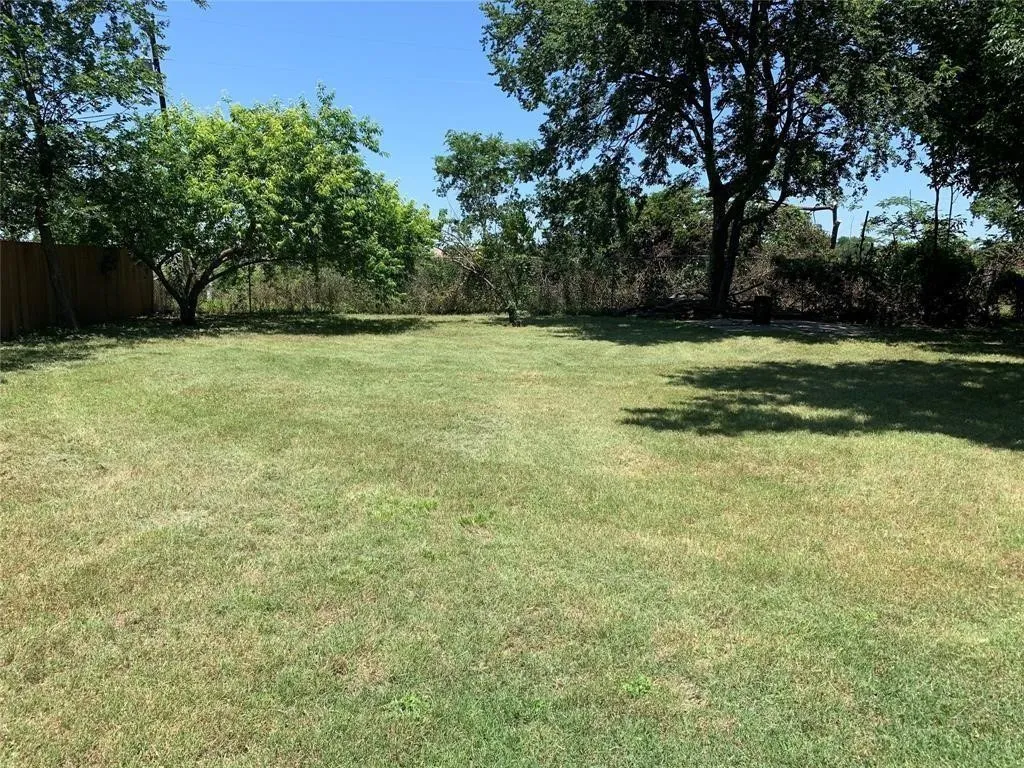 Expansive grass lawn featuring mature trees and a wood privacy fence