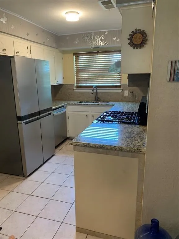 Kitchen featuring tiled flooring, granite countertops, white cabinetry, a built-in gas range, and a window with blinds