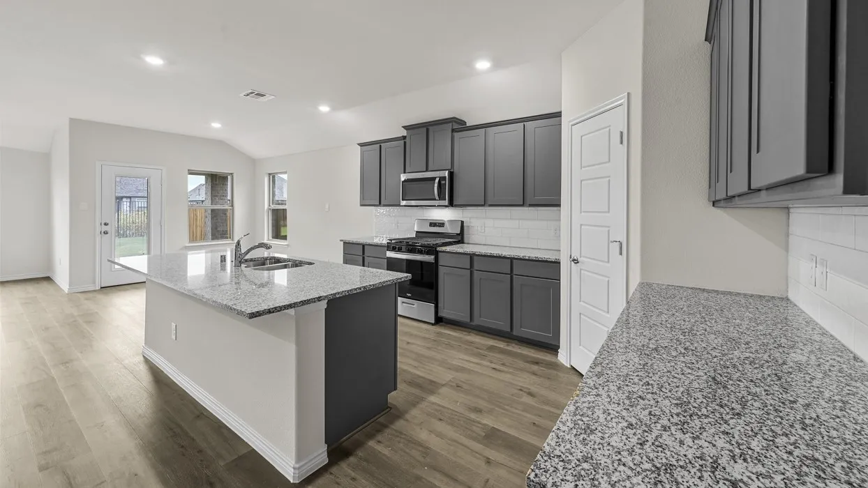 Kitchen featuring wood-finish flooring, an island with an undermount sink, granite countertops, gray cabinetry, and a subway tile backsplash