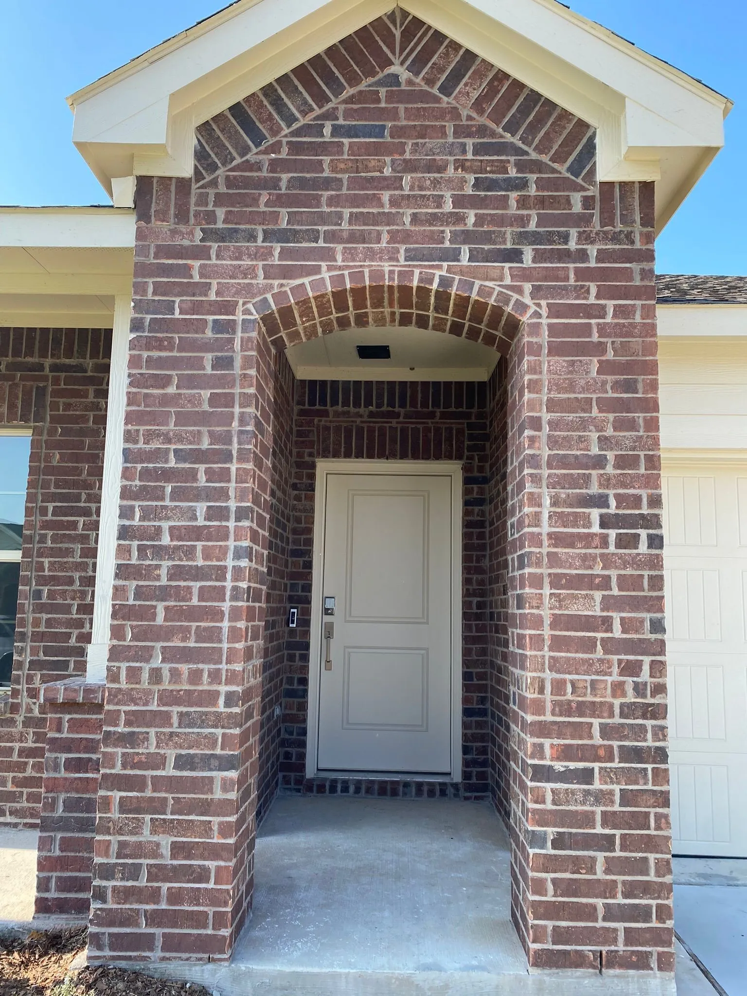 Brick exterior with a covered entry, arched doorway, and light-colored paneled door