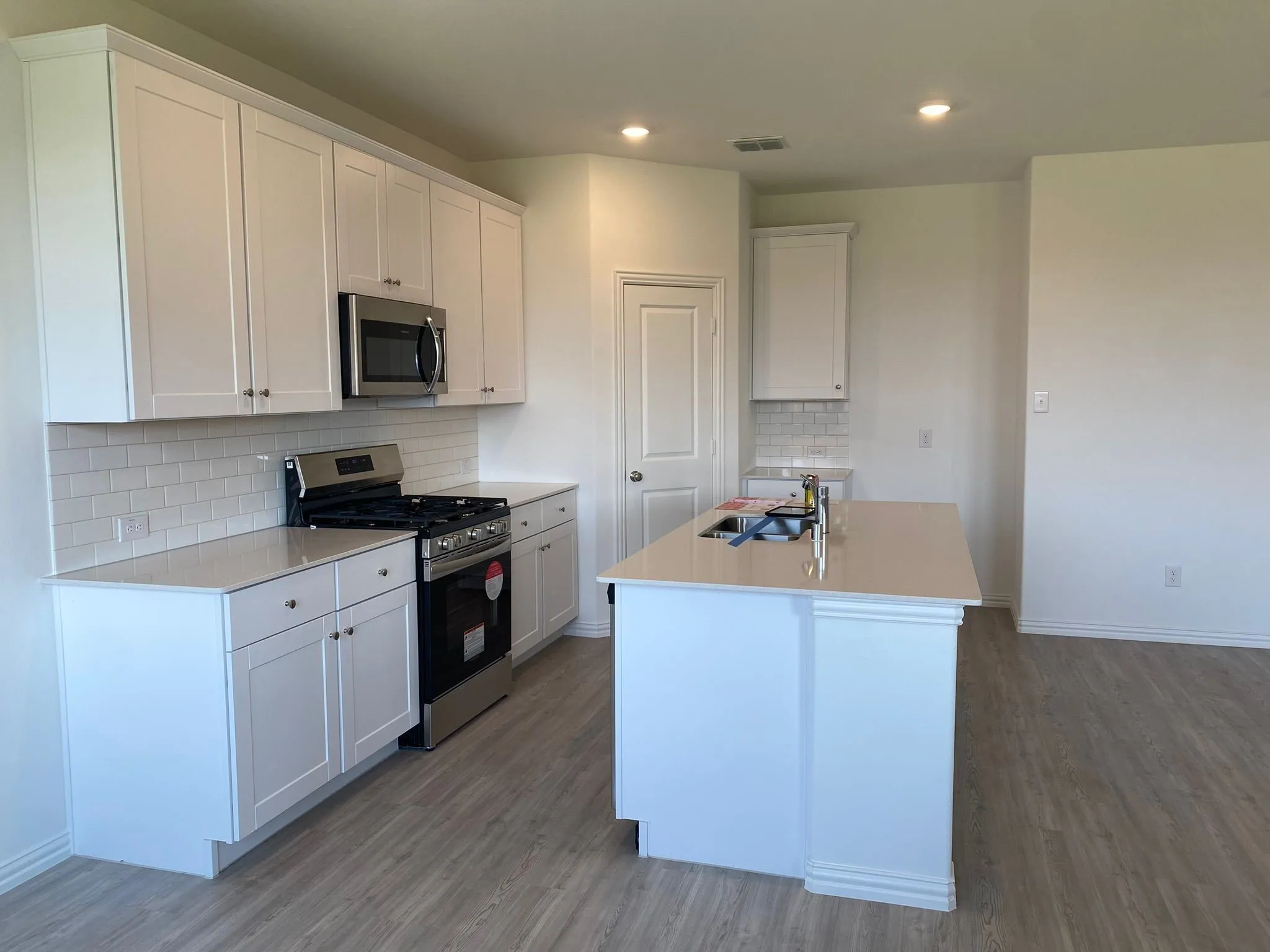 Kitchen featuring white shaker cabinetry, stainless steel appliances, light-toned countertops, subway tile backsplash, and a central island with an undermount sink