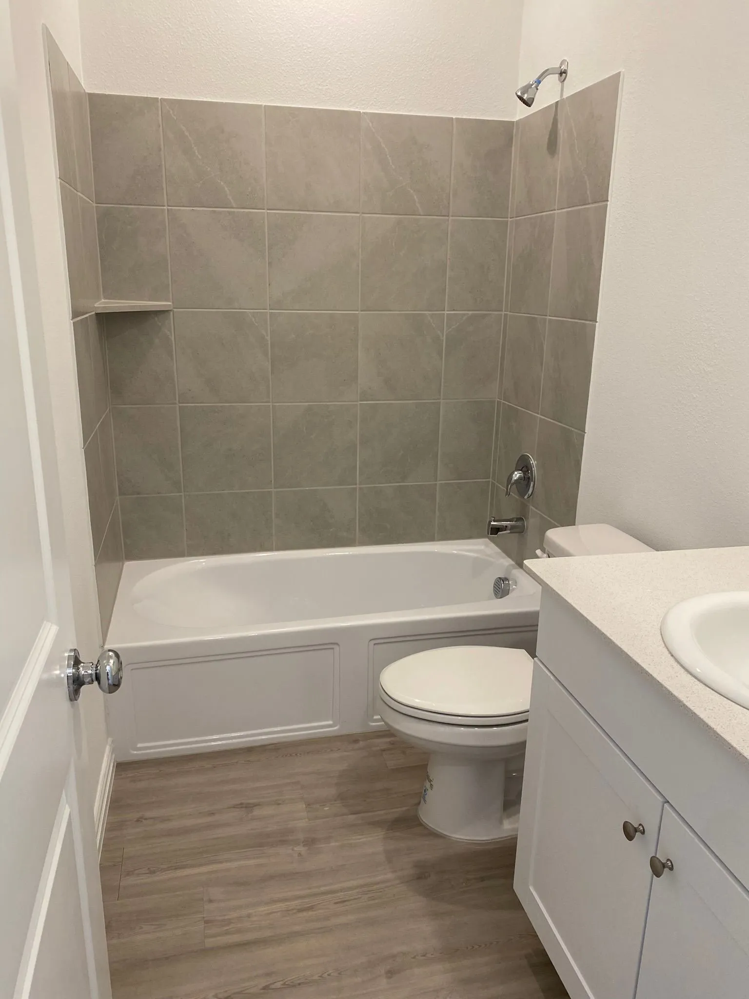 Bathtub with tile surround, built-in shelving, chrome fixtures, and a white vanity with integrated sink
