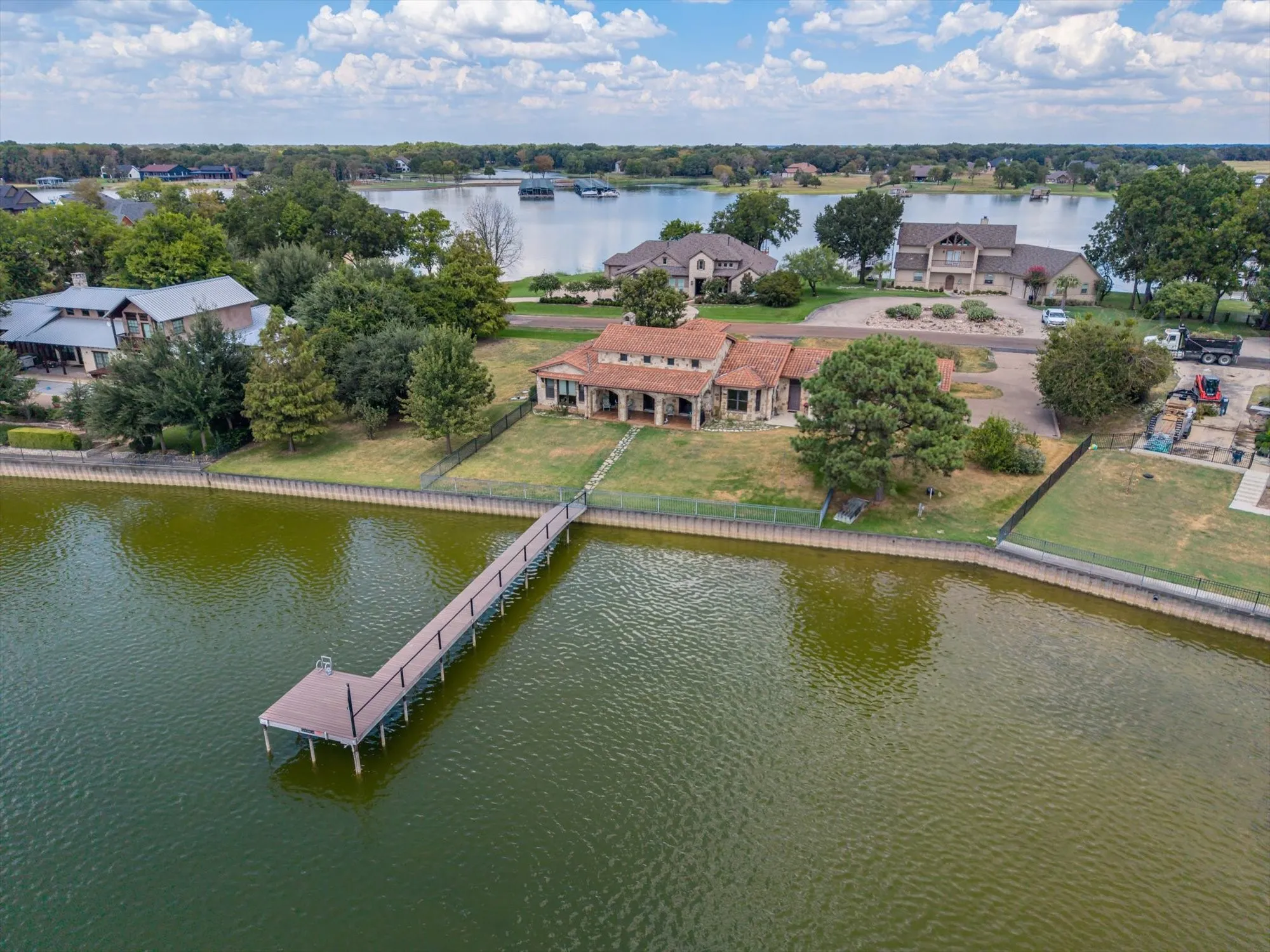 Lakeside property featuring a private dock extending into the water, mature trees, and a concrete-tiled roof