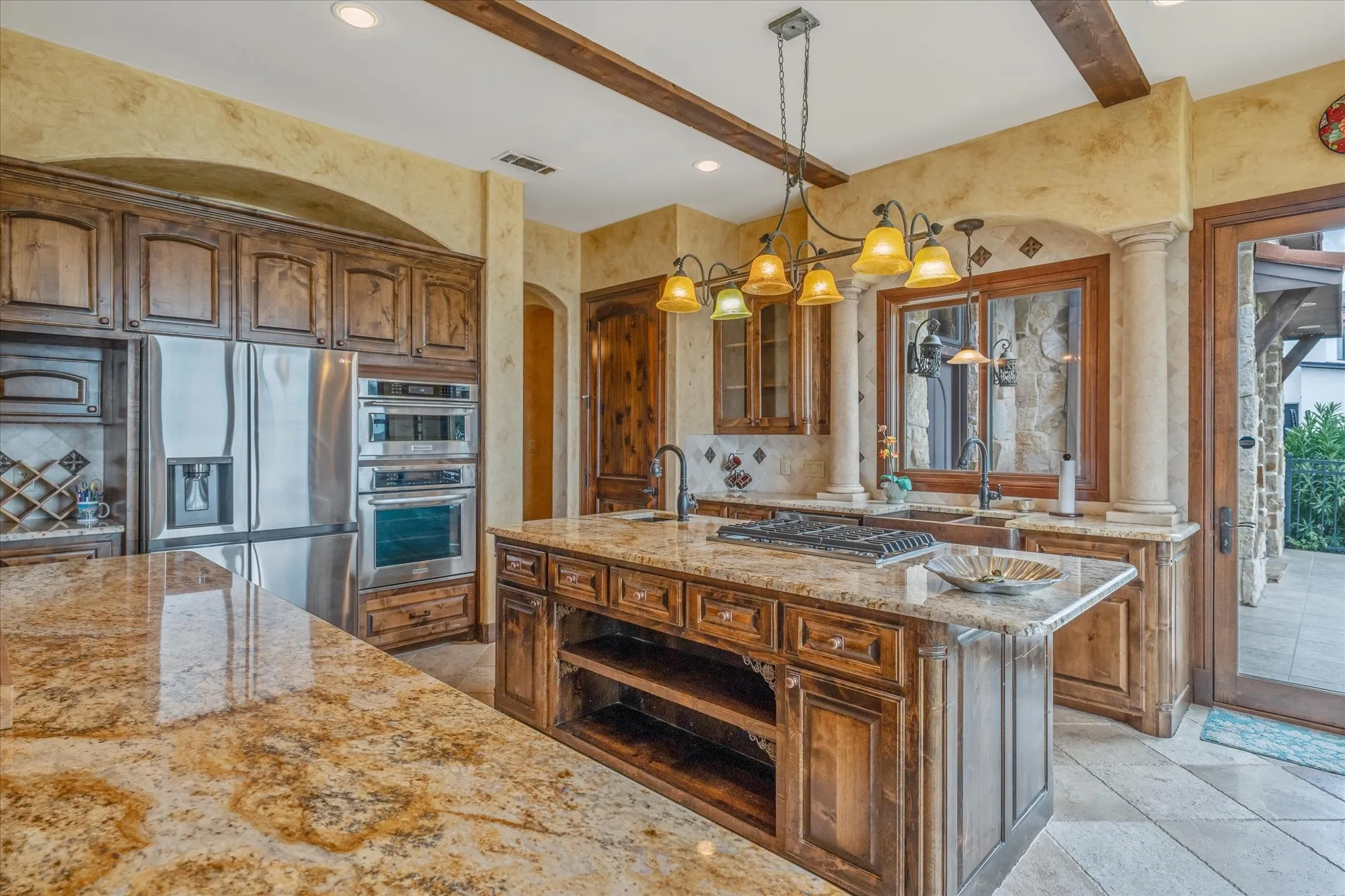 Gourmet kitchen featuring a built-in stainless steel refrigerator, double ovens, a gas range on a central island, and rich wood cabinetry with stone countertops