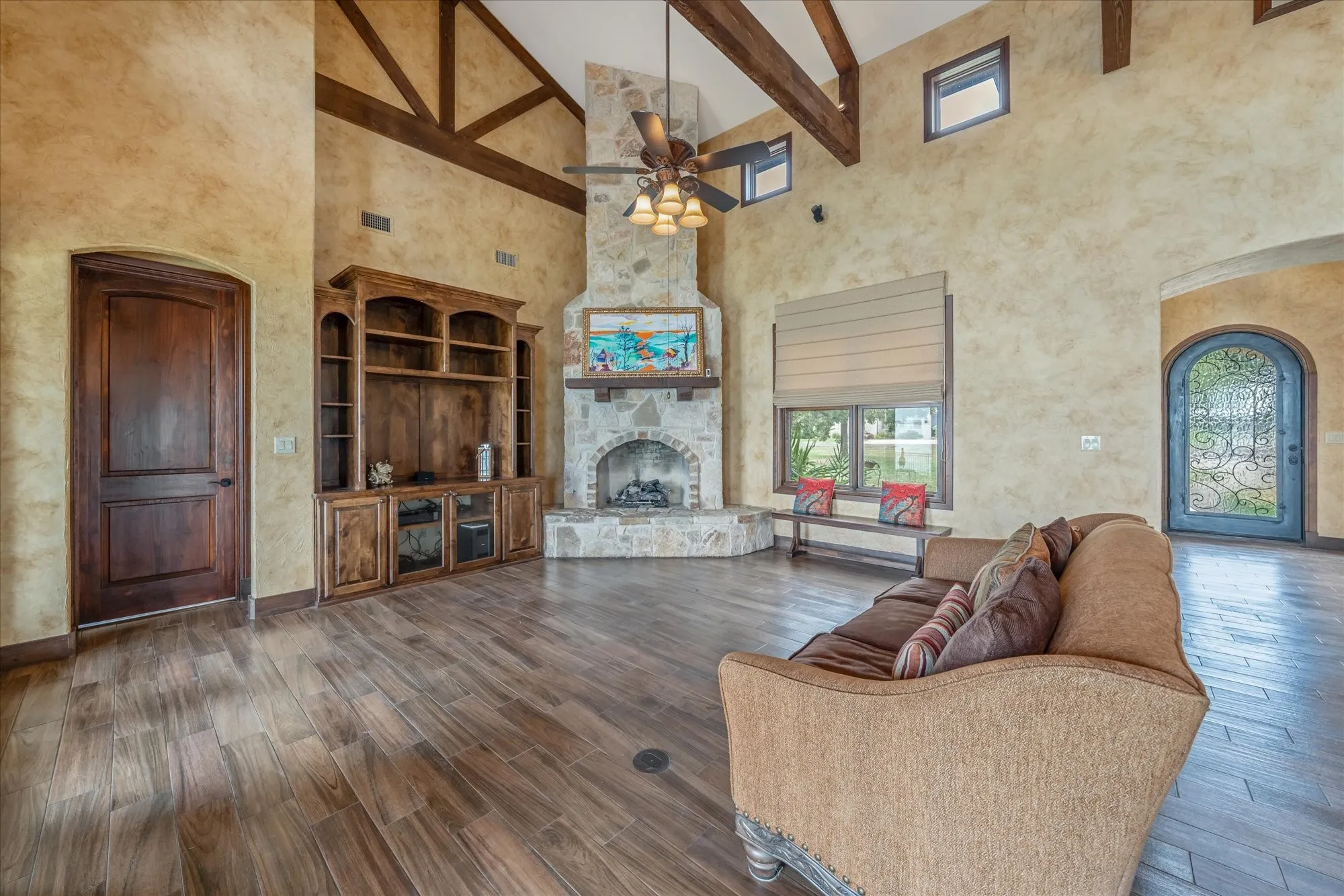 Vaulted ceiling with exposed wood beams, stone fireplace, wood-finish flooring, built-in cabinetry, and arched entryways