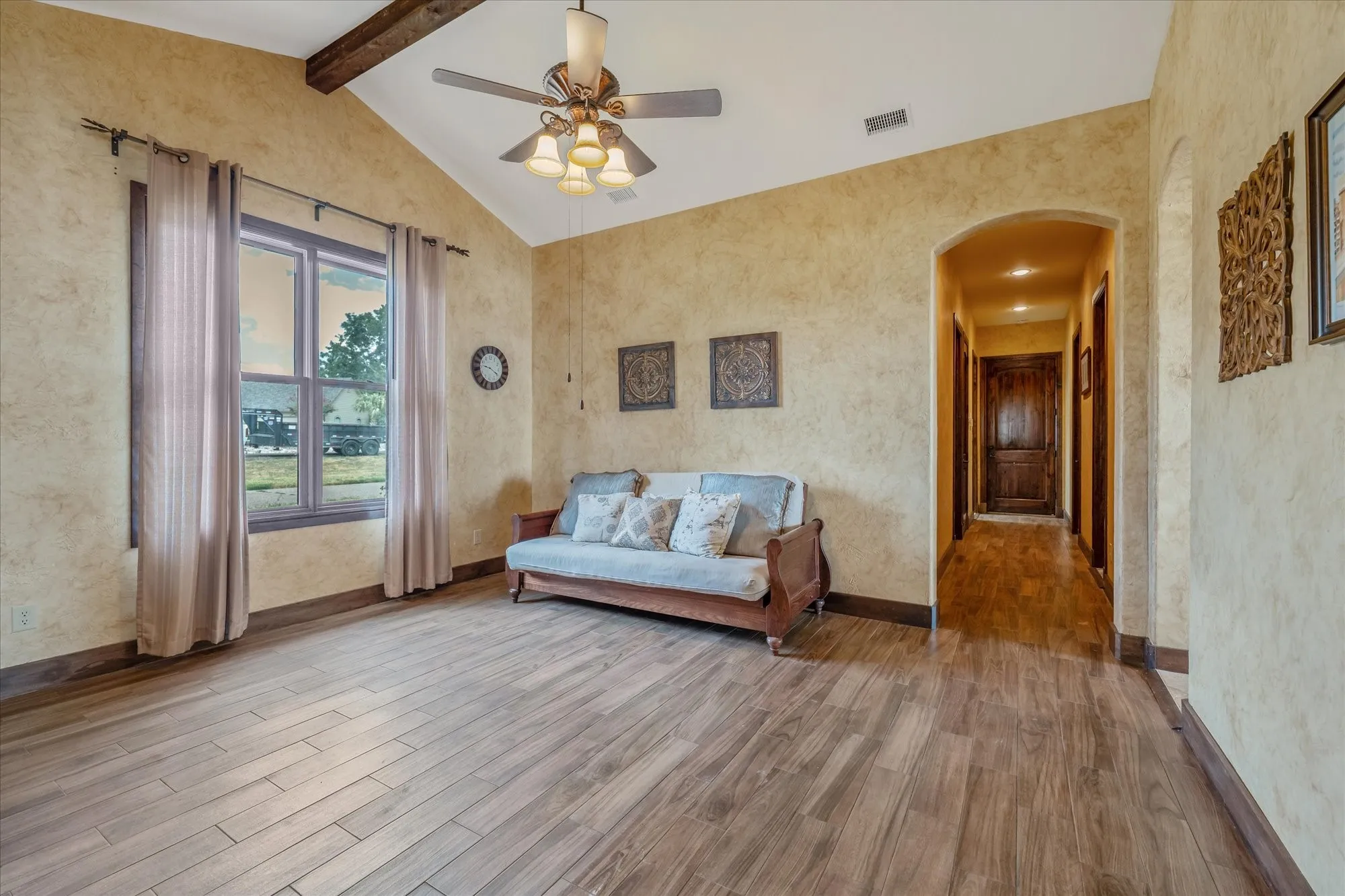 Vaulted ceiling with exposed wood beams, wood-finish flooring, textured wall finish, and an arched entryway